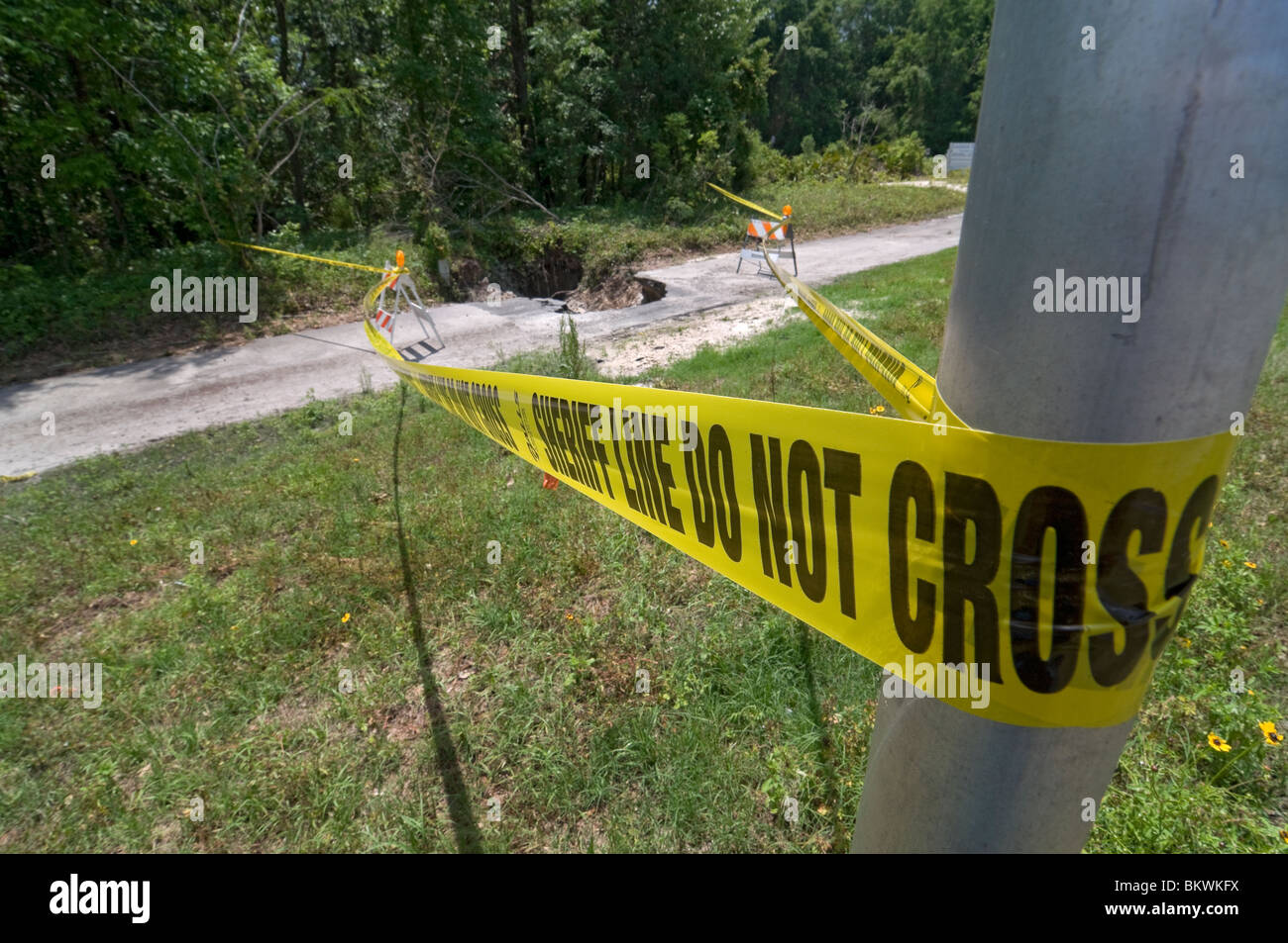 sheriff's yellow warning tape around sinkhole formed in footpath after heavy rainfall and stormy weather Branford Florida Stock Photo