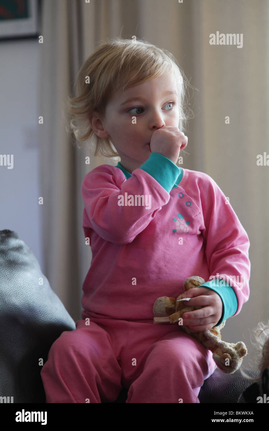 TWO YEAR OLD SUCKING THUMB: Two year old child baby girl suck sucking thumb sit sitting sat sofa couch soft toy hold Model released Stock Photo