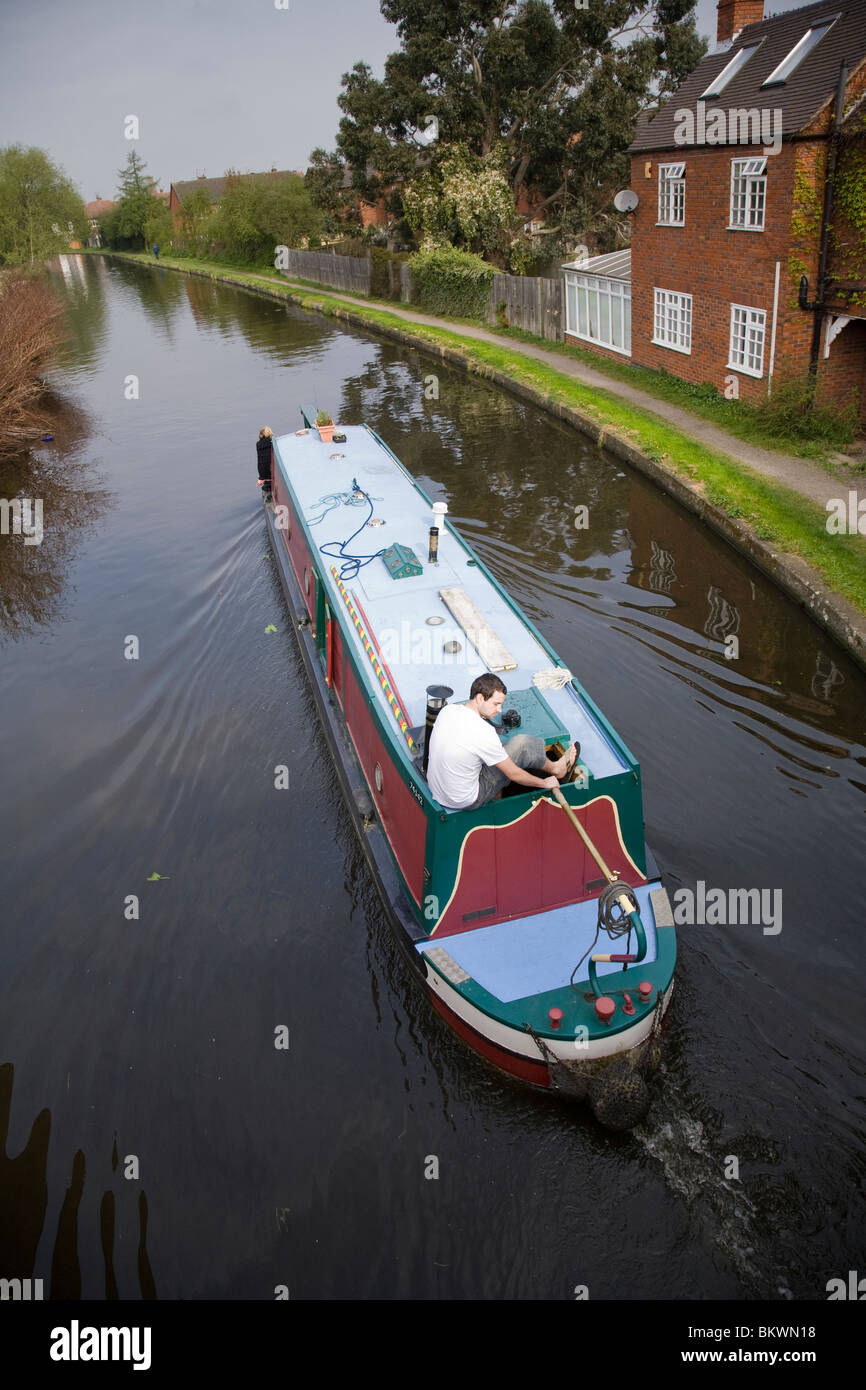 A man at the tiller of a narrow boat on the Grand Union canal ...