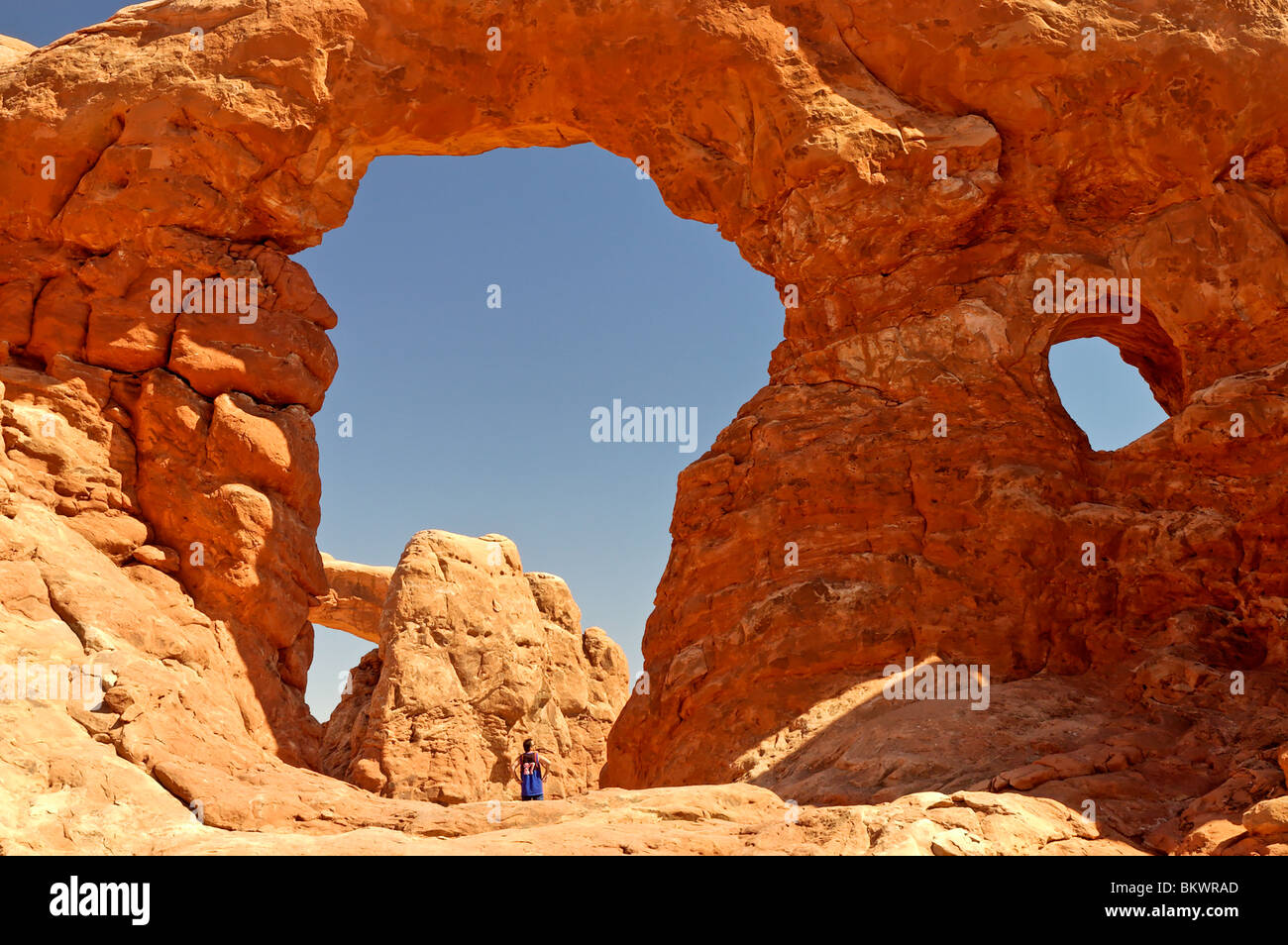 Stock photograph of a man in blue shirt standing under Turret Arch in Arches National Park Utah, USA. - Stock Image