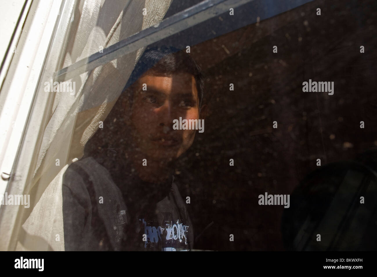 An undocumentd Central American migrant, traveling across Mexico to work in the US, peers through a window in Mexico City. Stock Photo