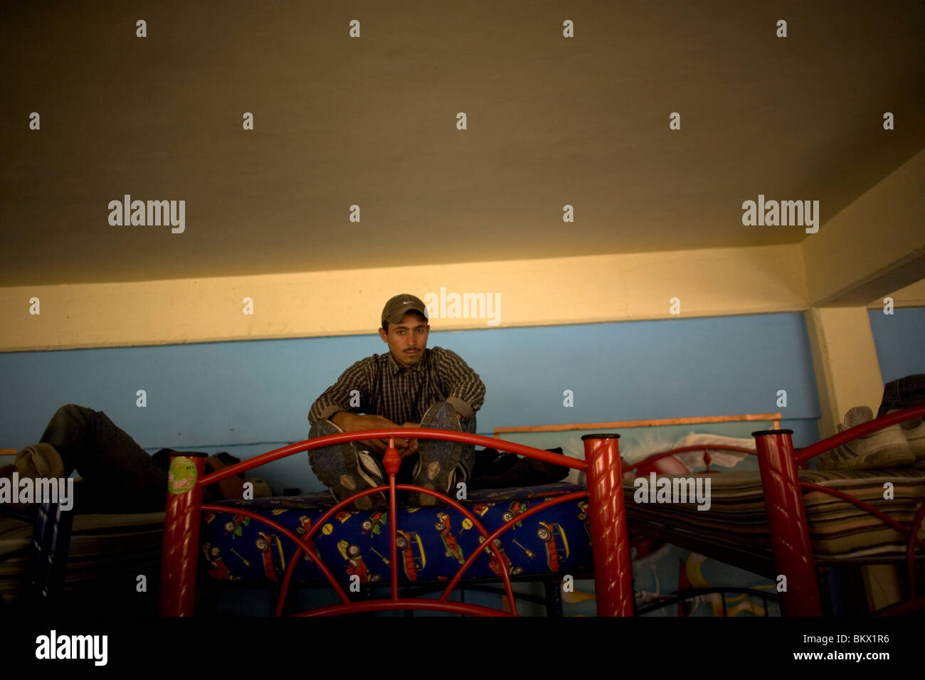 An undocumentd Central American migrant, traveling across Mexico to work in the US sits on a bed at a shelter in Mexico City. Stock Photo