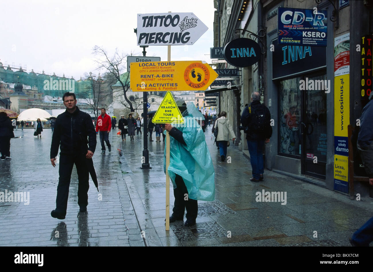 Krakow, April 2010 -- Man holds up advertisements for bike tours and a local tattoo and piercing shop. Stock Photo