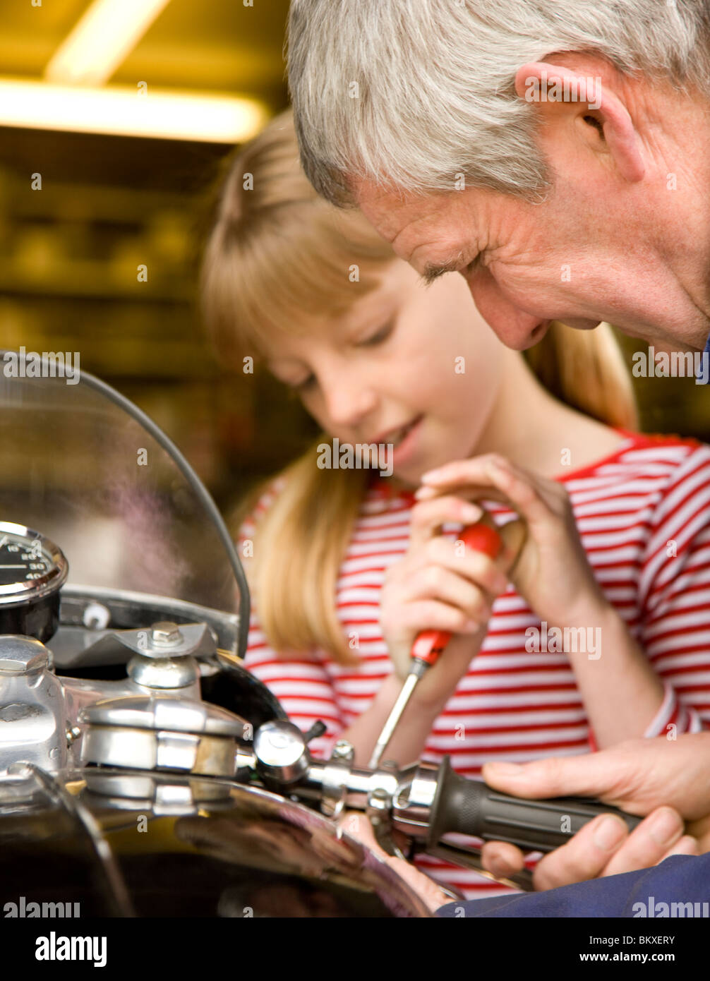 Young girl helping grandfather repairing motorbike handlebar with screwdriver Stock Photo
