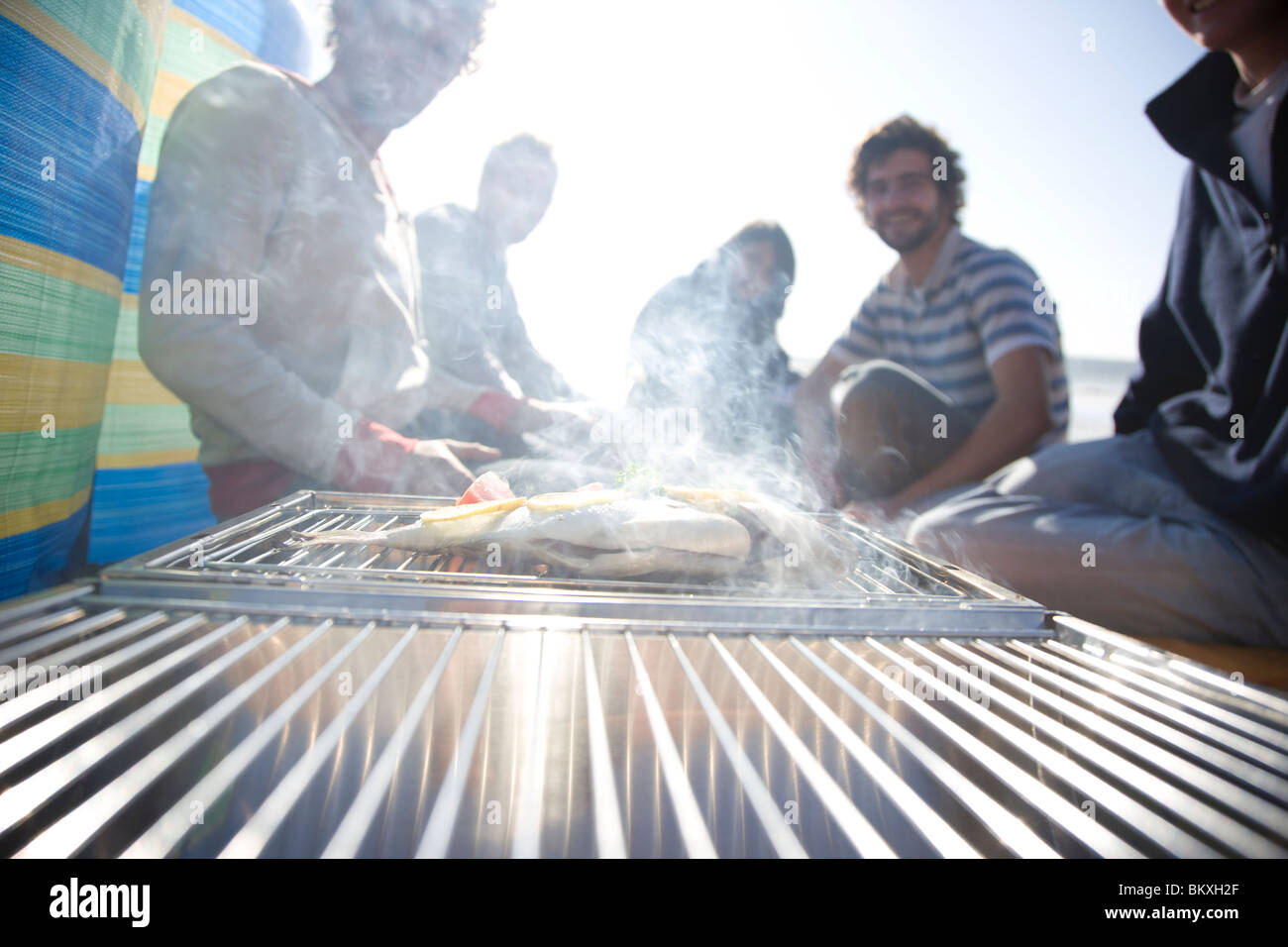 Group of friends sitting around a barbeque on the beach Stock Photo