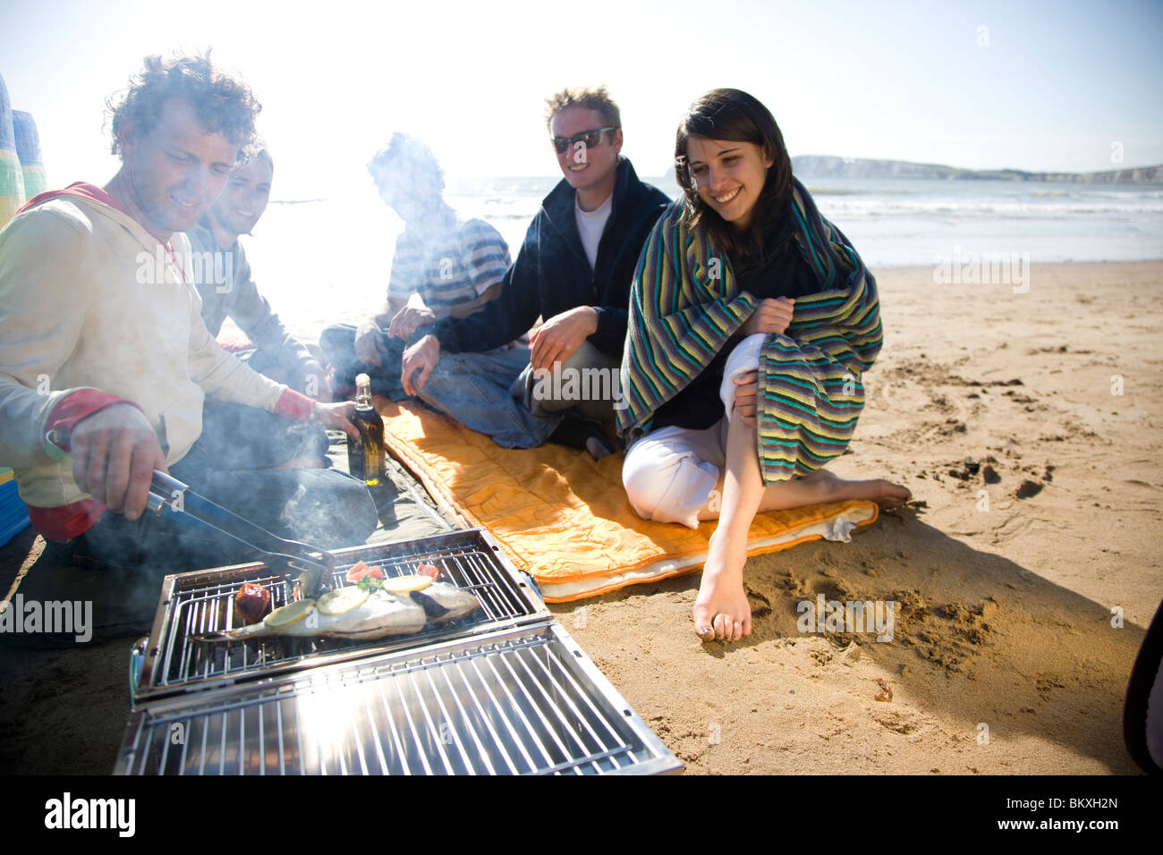 Group of friends sitting around a barbeque on the beach Stock Photo