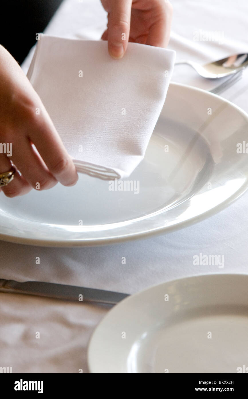 Close up of a waitress's hands arranging a napkin on a restaurant table Stock Photo