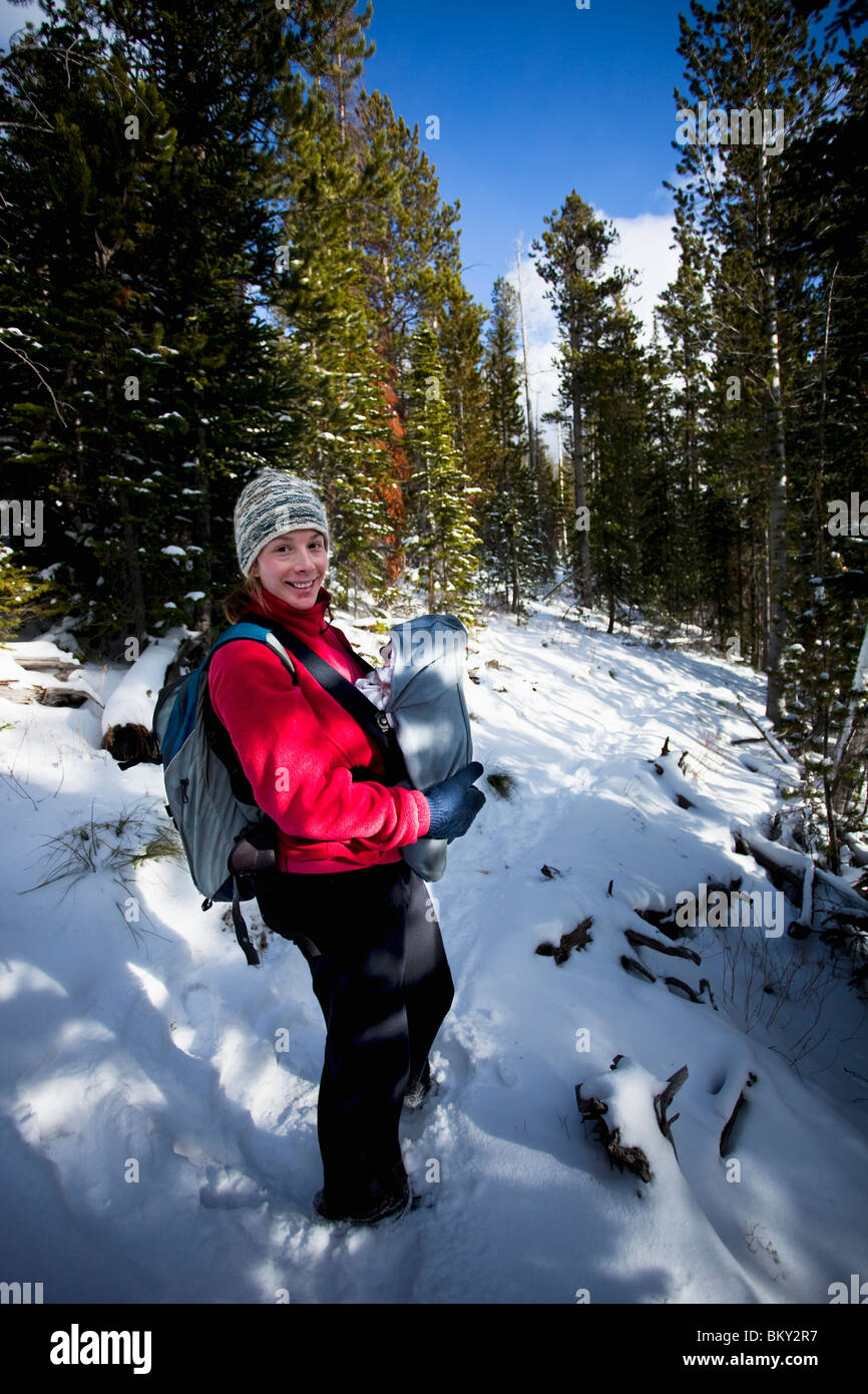 Mother and newborn baby in a front carrier on a snowy hiking trail in