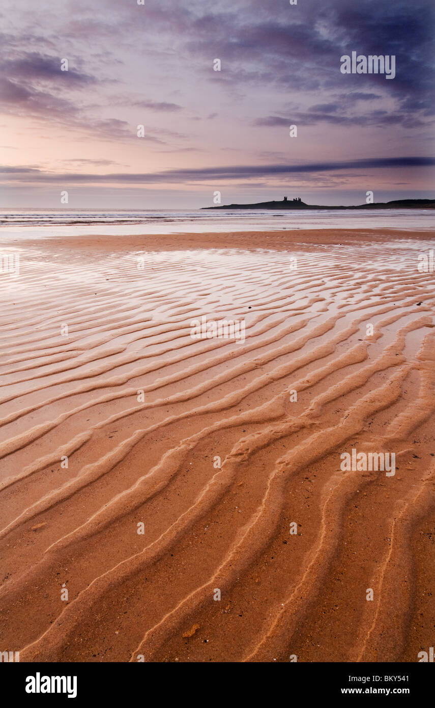 Ripples in the sand with Dunstanburgh Castle in the distance at Dawn Stock Photo