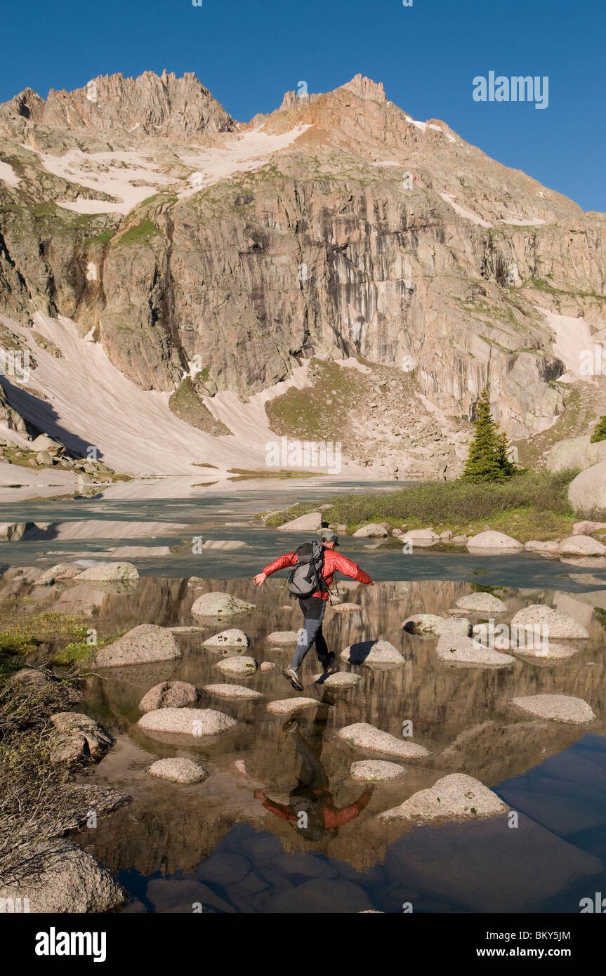 A man jumping across rocks over a lake in the Weminuche Wilderness, San Juan National Forest, Colorado. Stock Photo