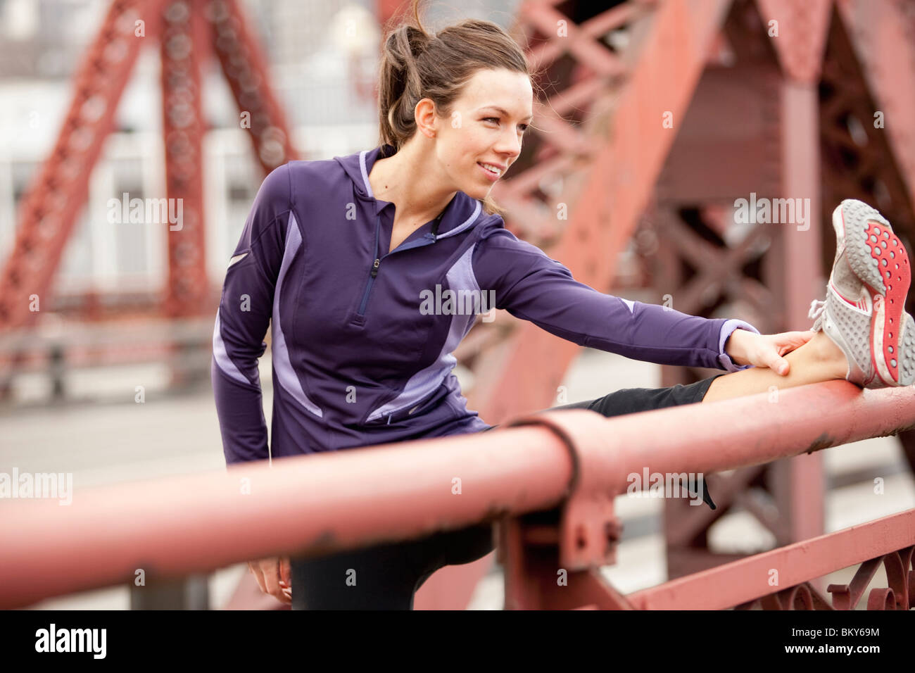 An athletic female in a purple jacket stretching along a bridge in Portland, Oregon. Stock Photo