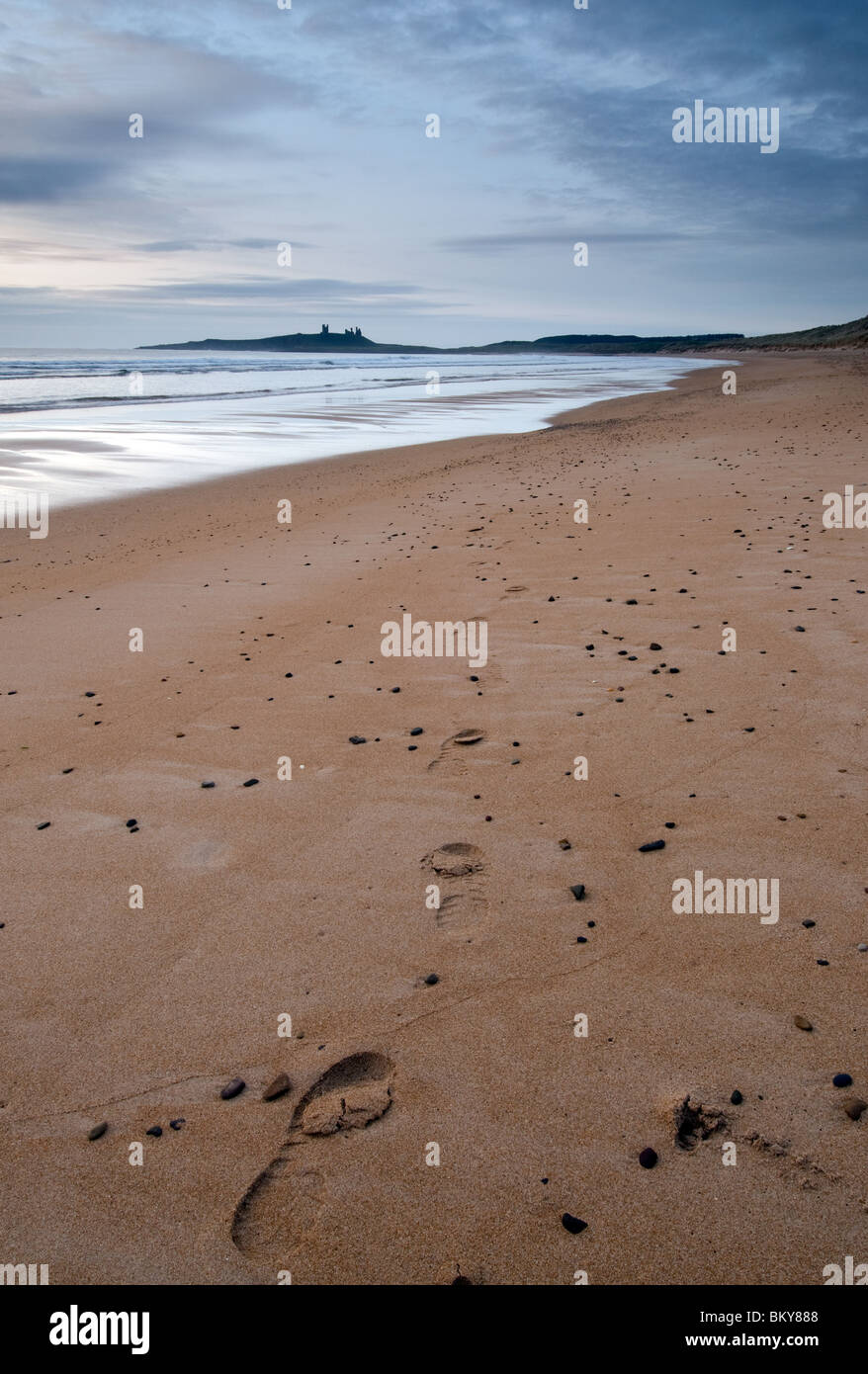 Footprints in the sand at Embleton Bay with Dunstanburgh Castle in the distance Stock Photo