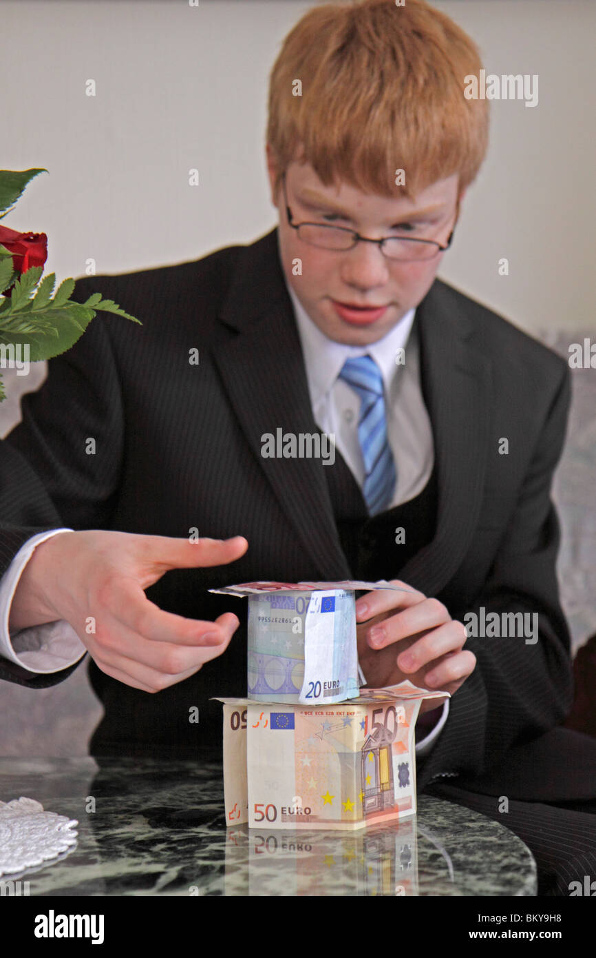 teenage boy building a house of cards from his money at his confirmation party Stock Photo