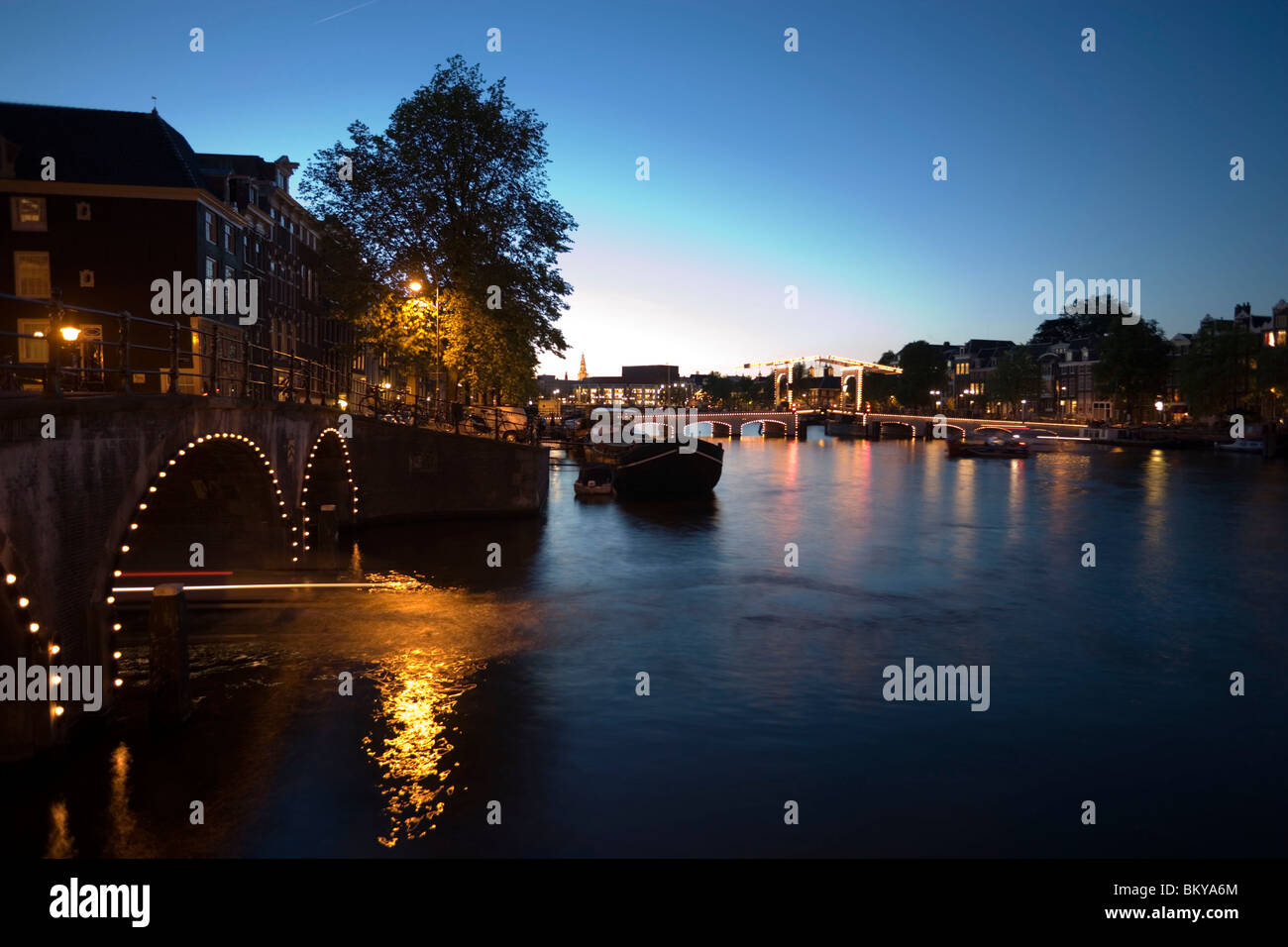 Boats, Magere Brug, Amstel, View over illuminated Magere Brug Skinny Bridge, to Stopera and Zuiderkerk at night, Amsterdam, Holl Stock Photo