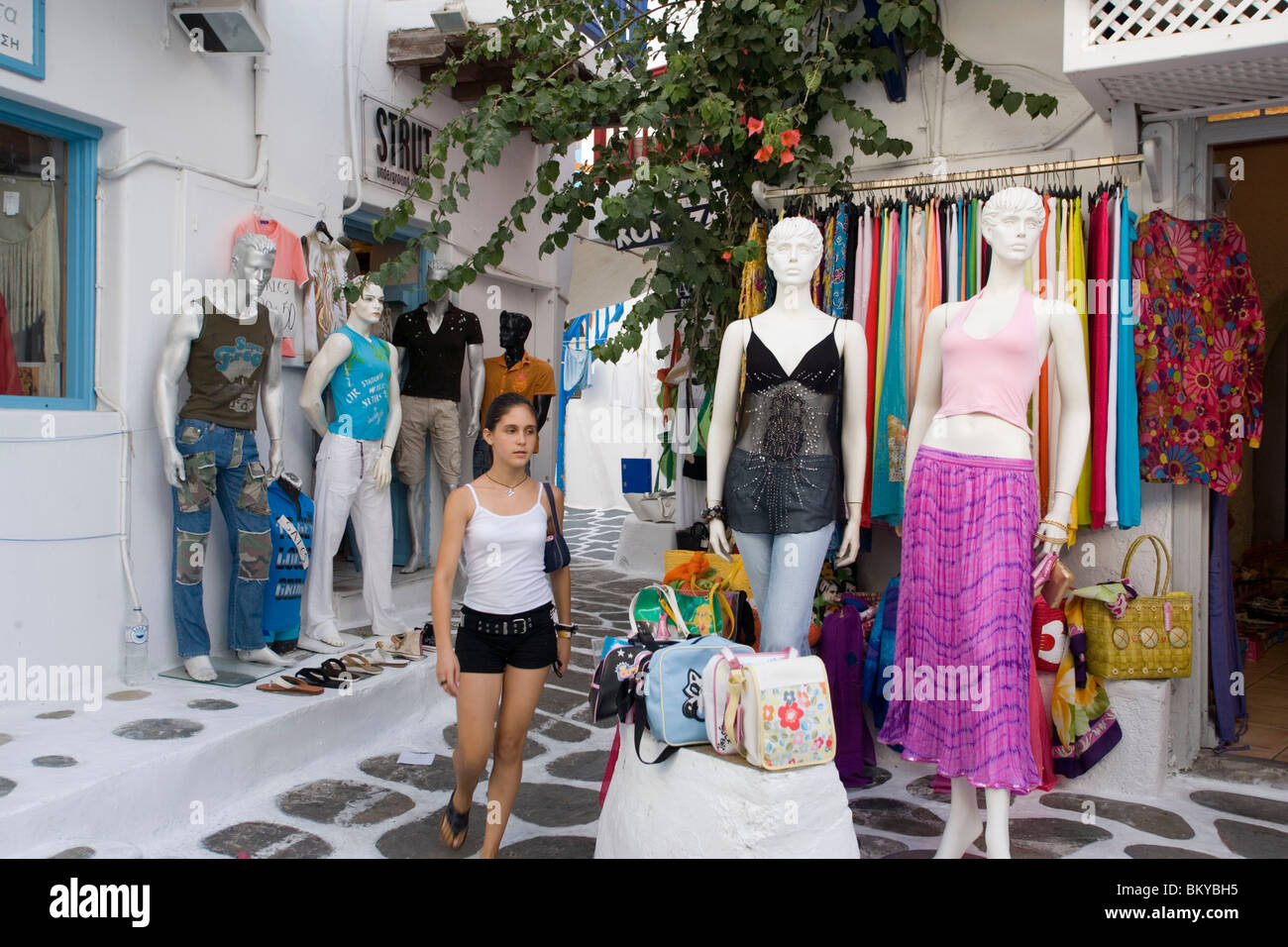 Girl passing a open clothes shop at shopping street, MykonosTown