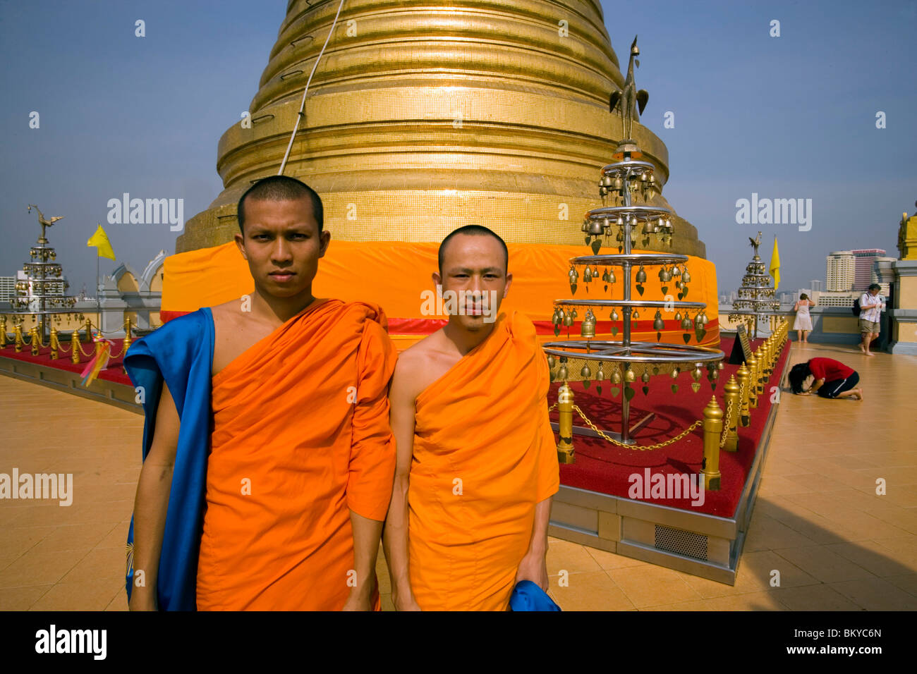Two monks in front of gilded Chedi, housed a Buddha relic of the Wat Saket on the Golden Mount, woman praying in background, Ban Stock Photo