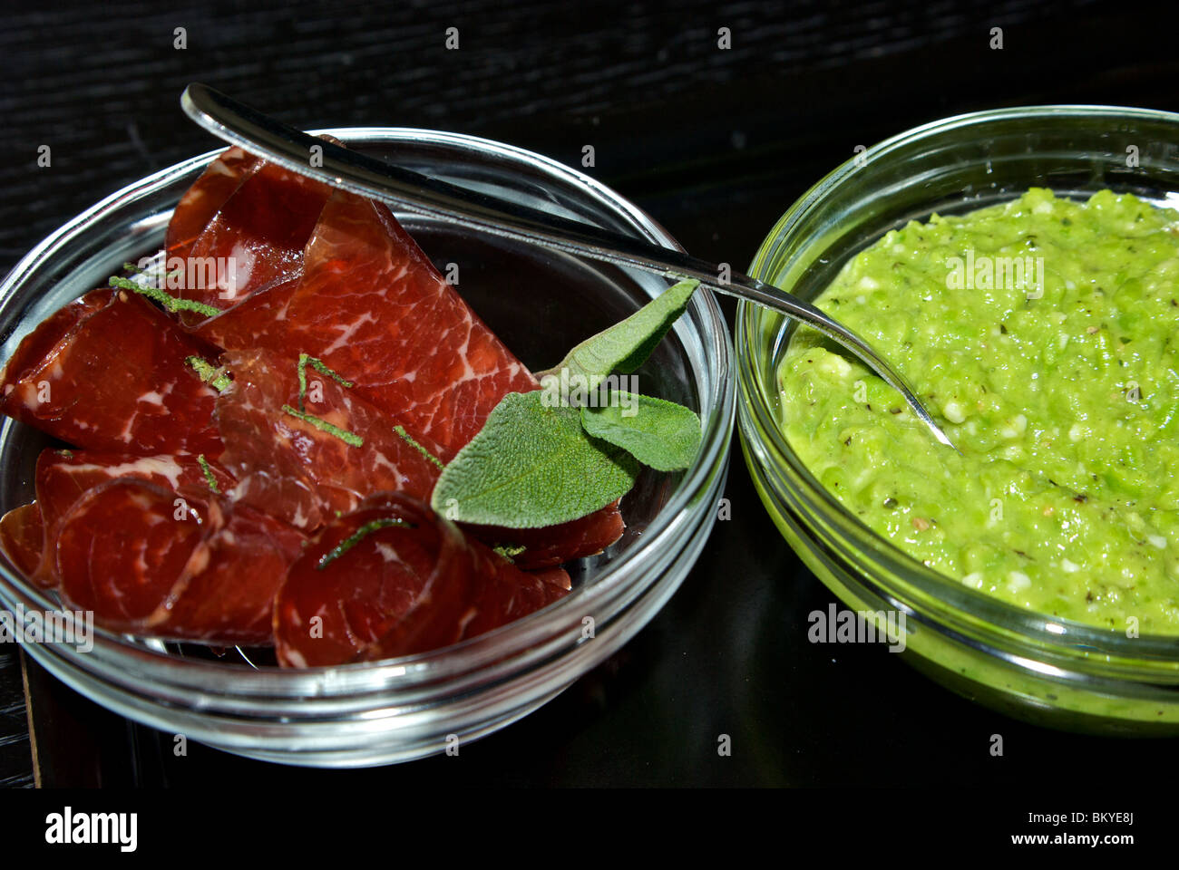 Rolled slices prosciutto ham sage leaves garnish spoon in bowl of green