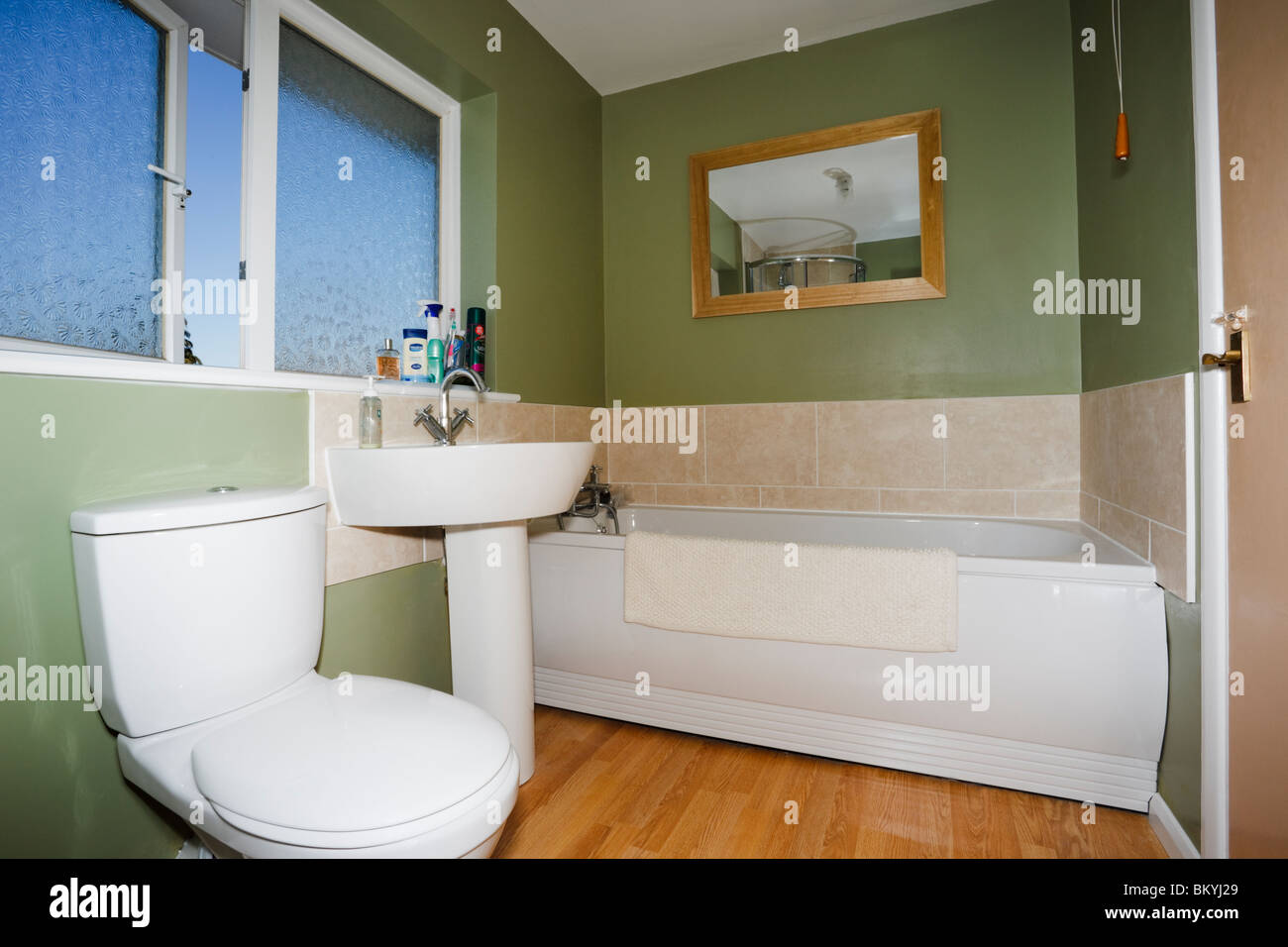 Small bathroom restroom with green walls and white suite with ceramic toilet, washbasin and bathtub. England, UK, Britain. Stock Photo
