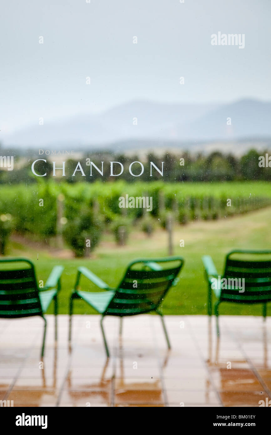 Domaine Chandon winery with green chairs on rainy patio overlooking vines, bushes, trees and hills in the background. Stock Photo