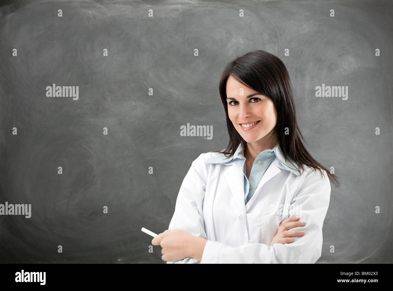 portrait of mid adult teacher with arms folded against blank blackboard. Copy space Stock Photo