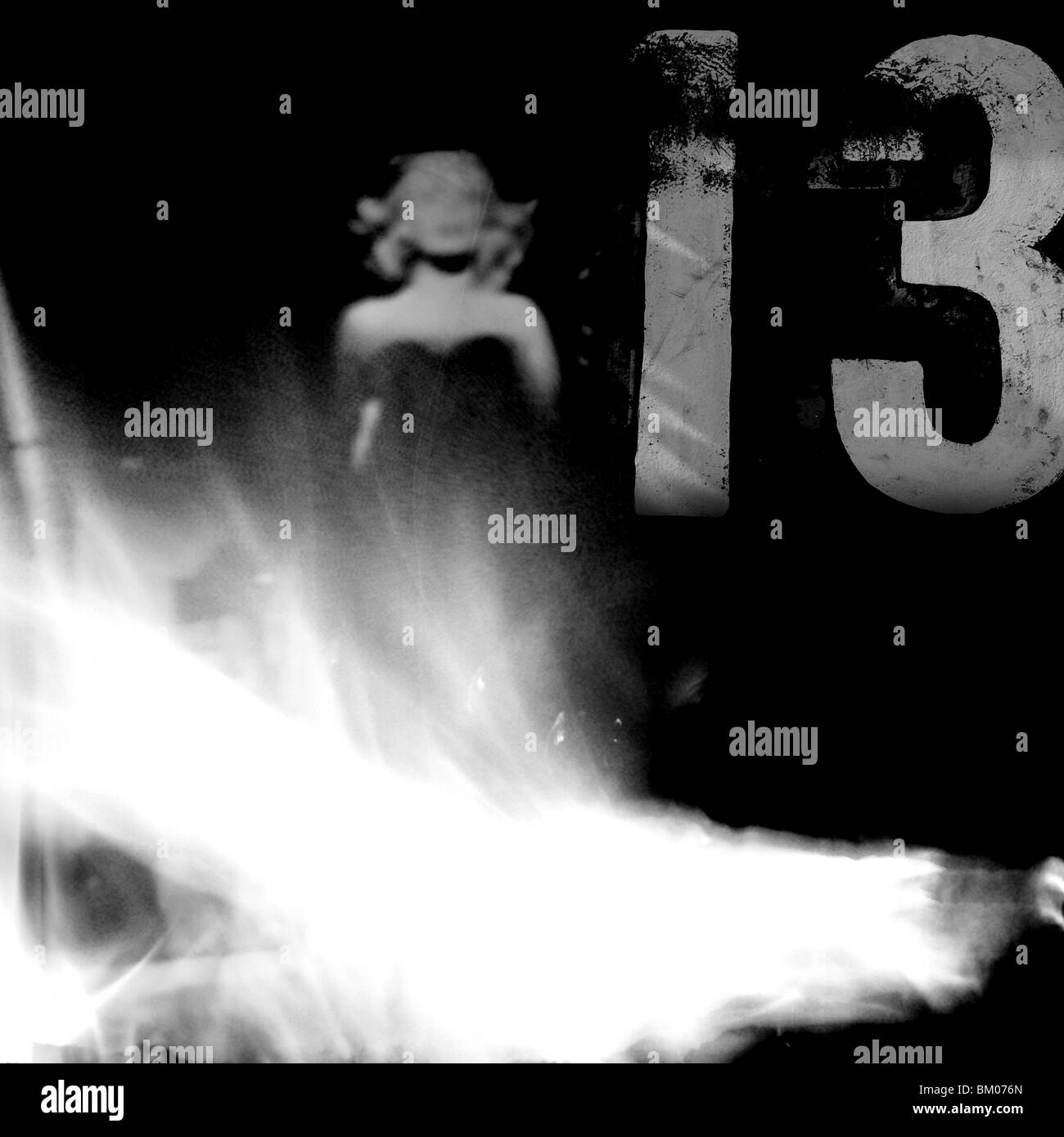 a woman in an evening dress stands behind a wall of flames and in front of the number 13 Stock Photo