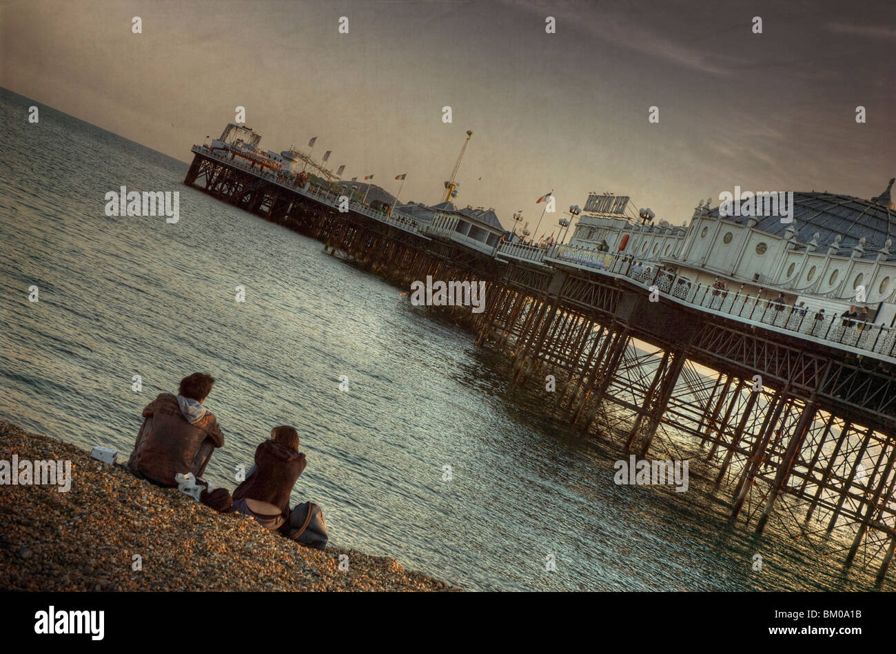 A young couple sitting on the beach beside pier in the evening at Brighton East Sussex England Stock Photo
