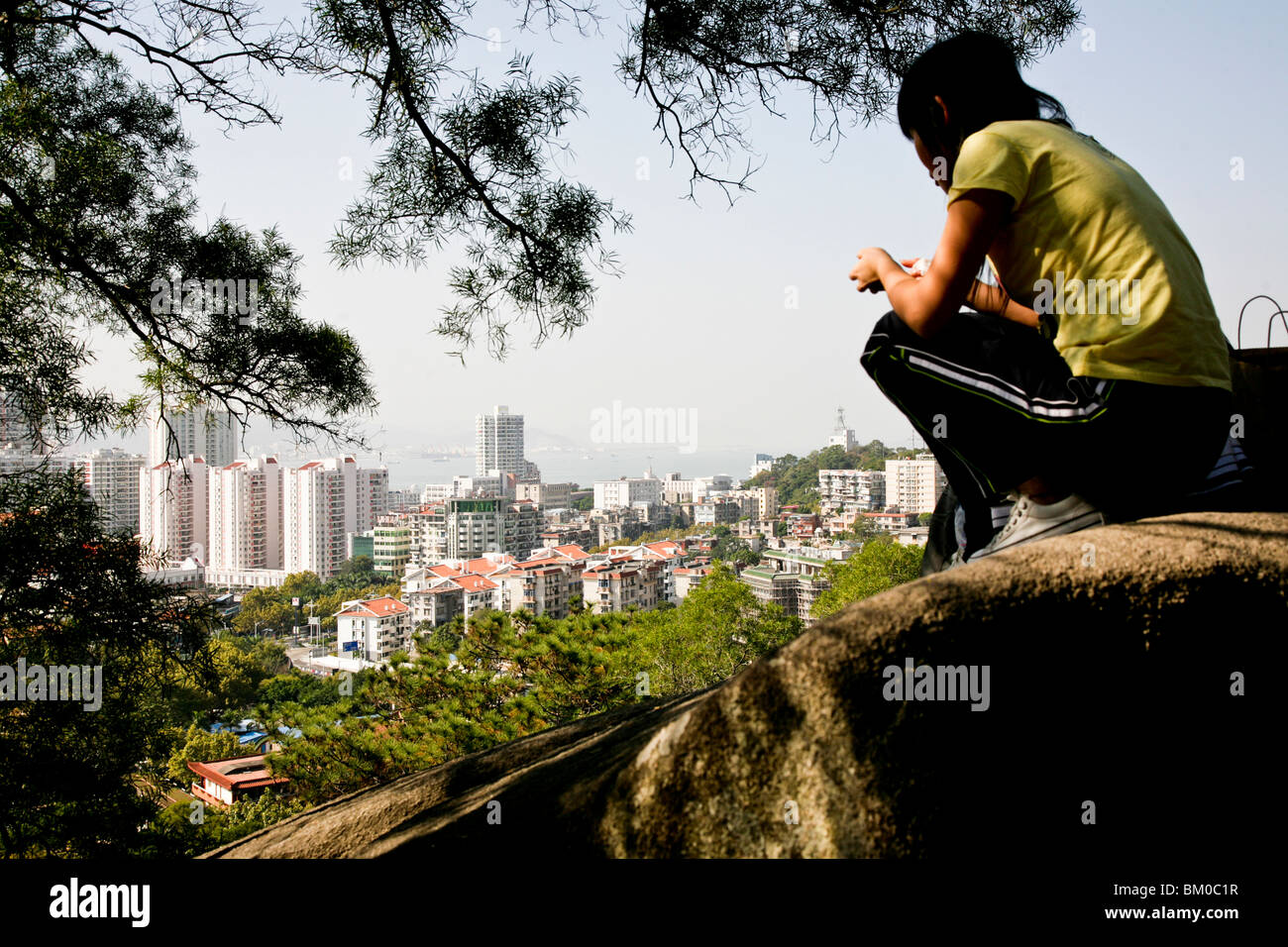Young woman on a rock with view over the city, district Siming, Xiamen, Fujian province, China, Asia Stock Photo