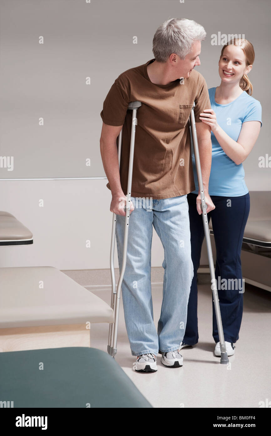 Physiotherapist assisting a patient in walking with crutches Stock