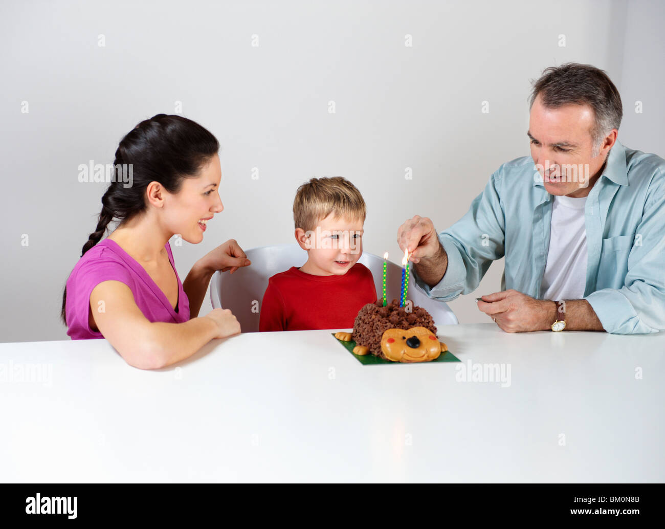 Couple lighting candles on cake for son Stock Photo
