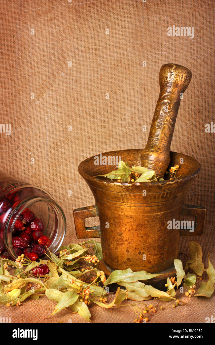 Old bronze mortar with dry herbs and rose hips on sacking background