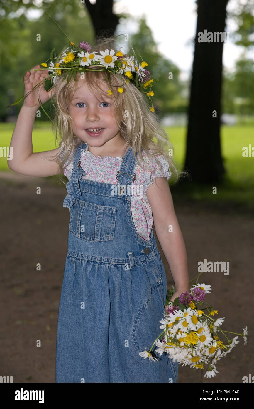 little smiling girl in a wreath and with a bouquet looks in the camera ...