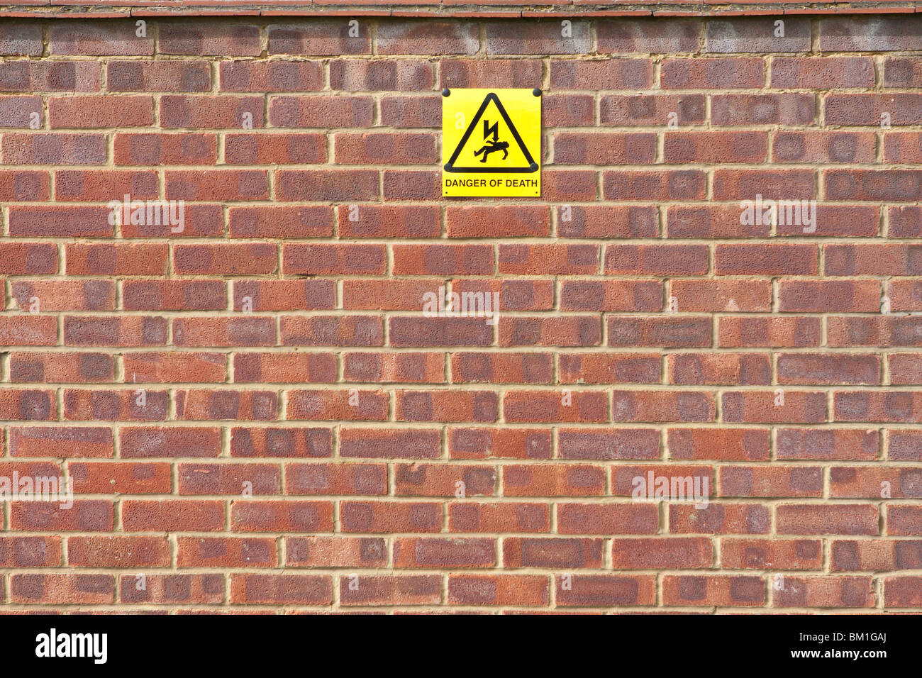 Yellow warning sign on red brick wall Stock Photo