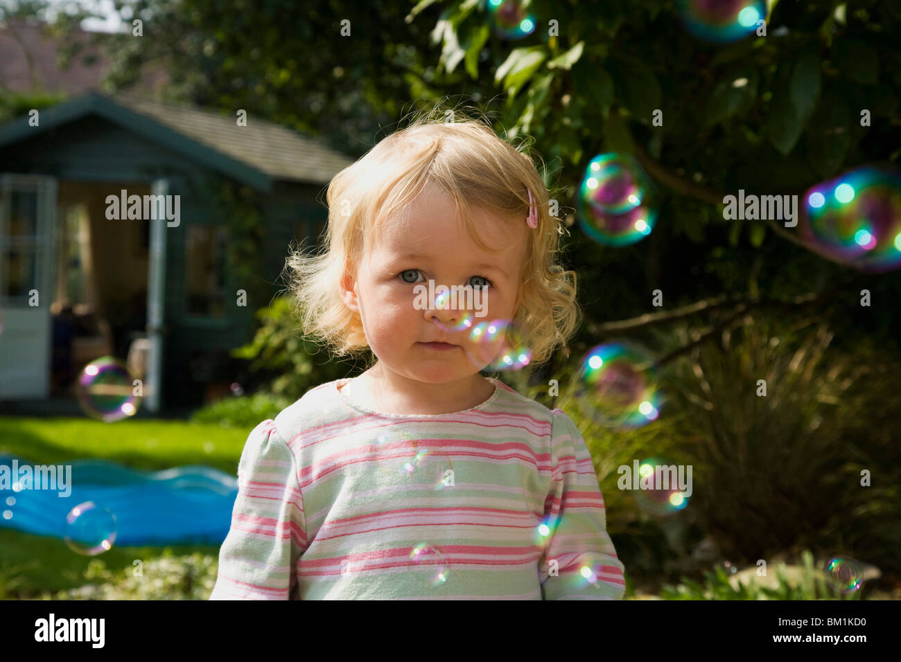 Young white caucasian 18 month old female girl toddler watching bubbles in garden England UK GB British Isles Europe EU Stock Photo