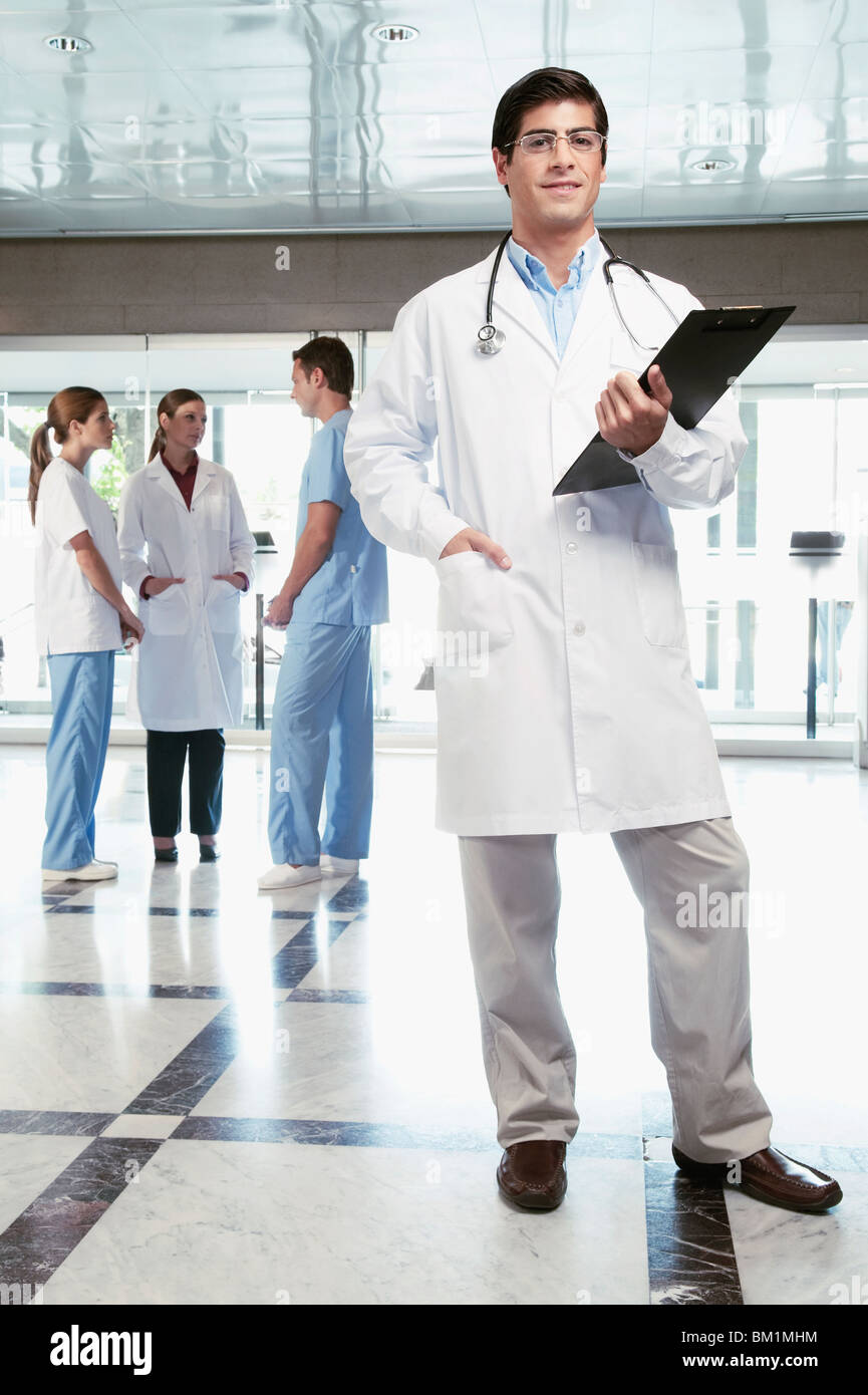 Doctor holding a clipboard with his colleagues discussing in the background Stock Photo