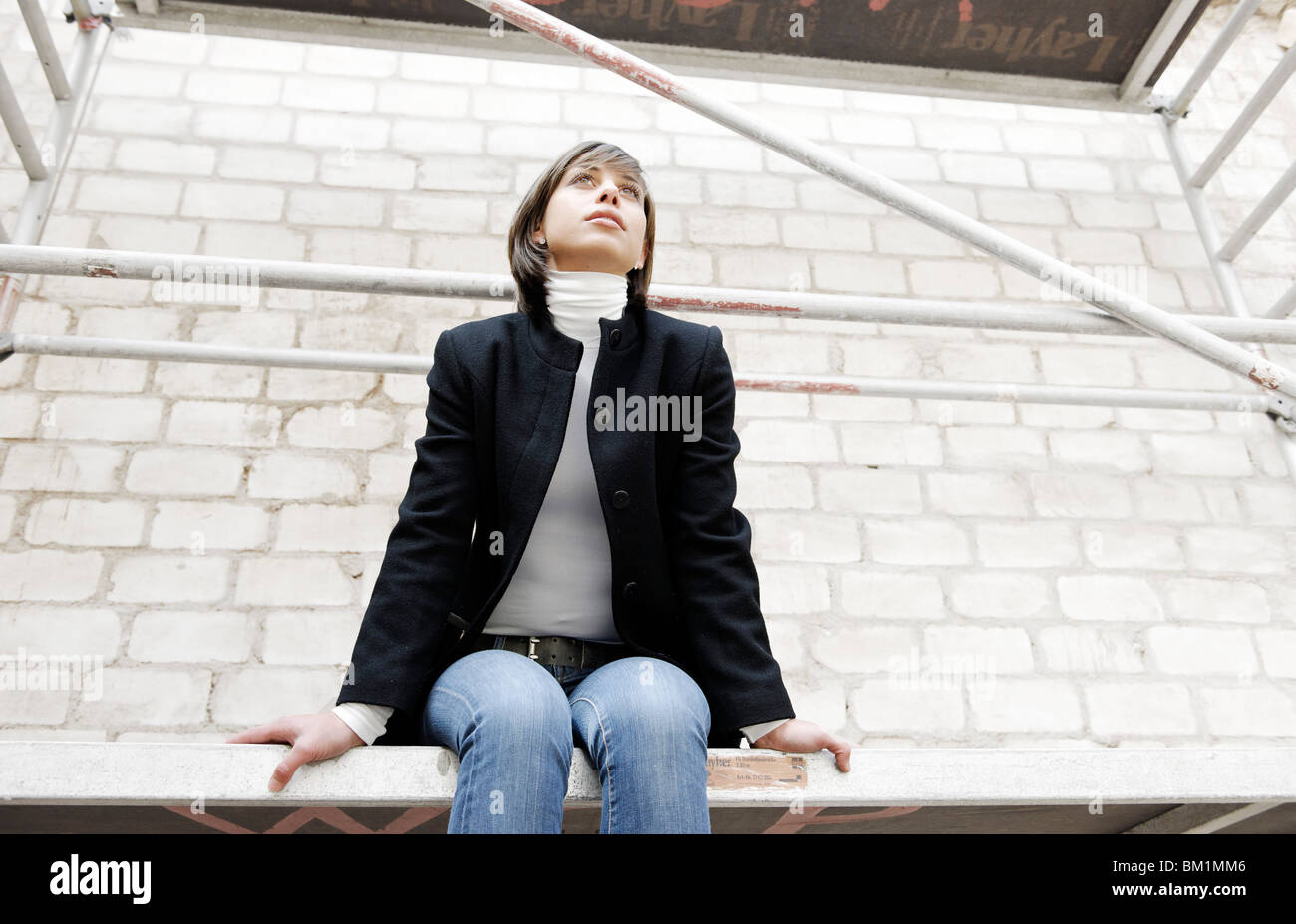 Young brunette woman, 25 years, sitting on scaffolding, looking thoughtful Stock Photo