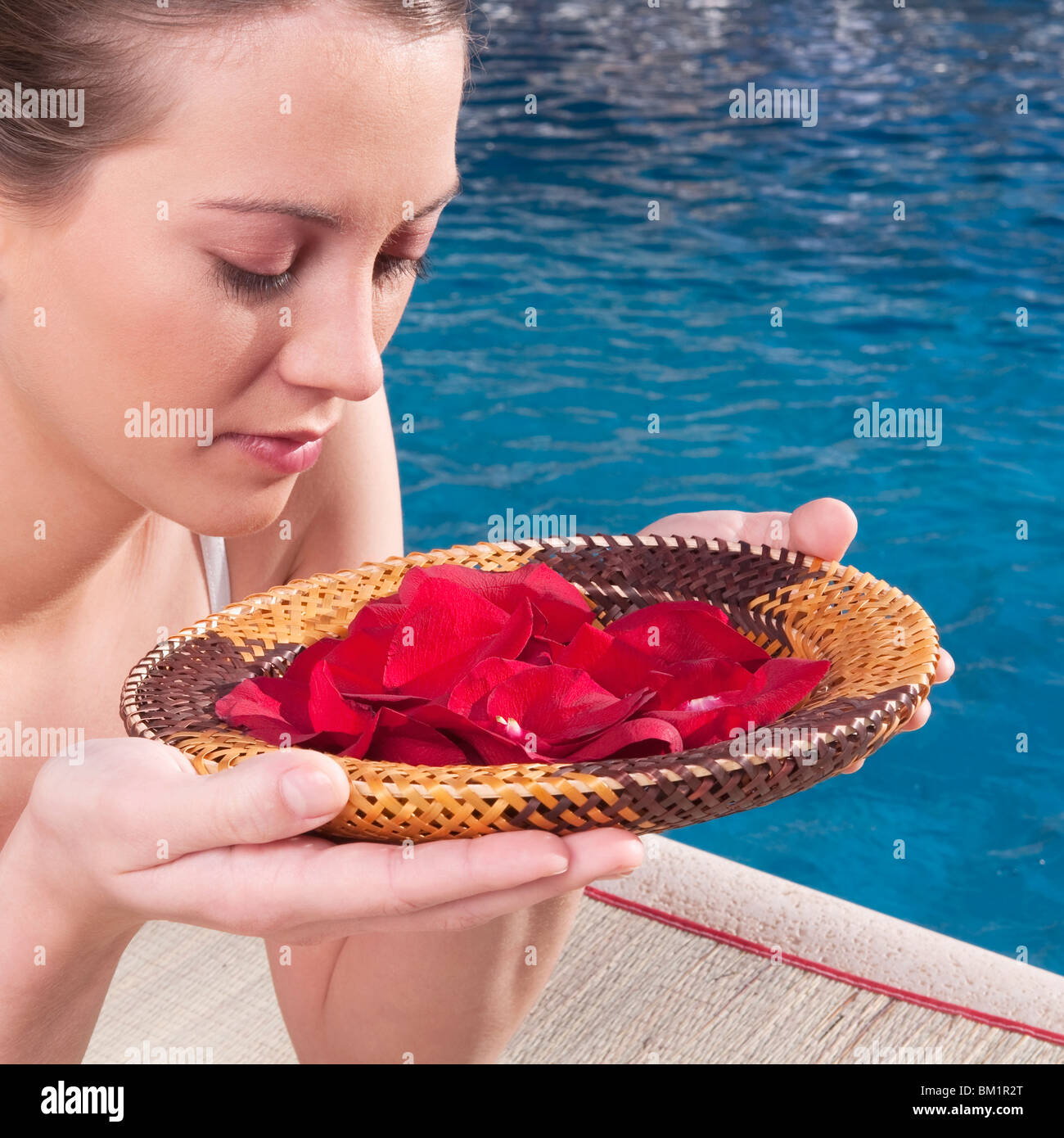 Woman holding a plate of rose petals at the poolside Stock Photo