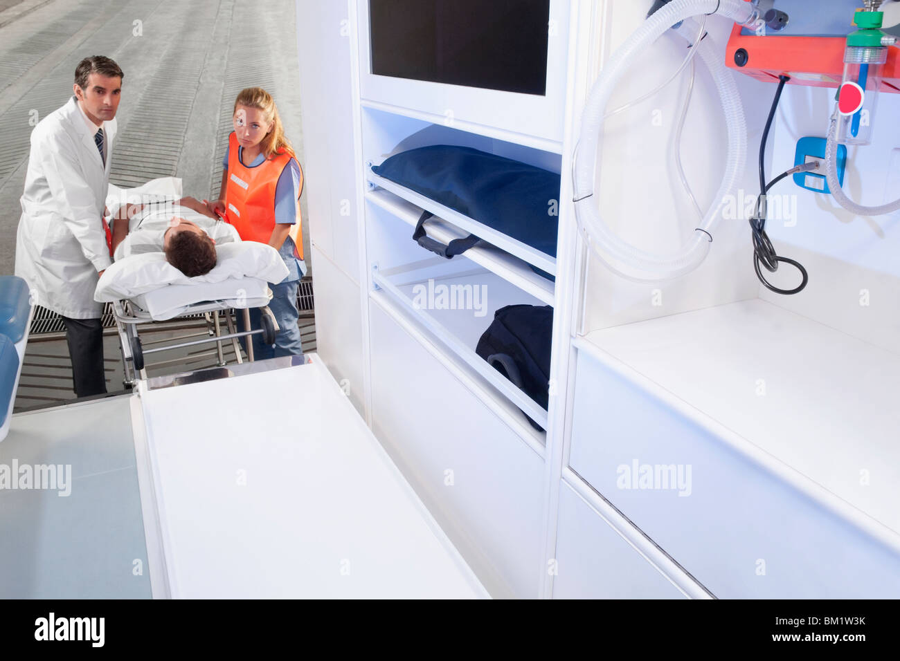 Paramedics leading a patient on a gurney into an ambulance Stock Photo