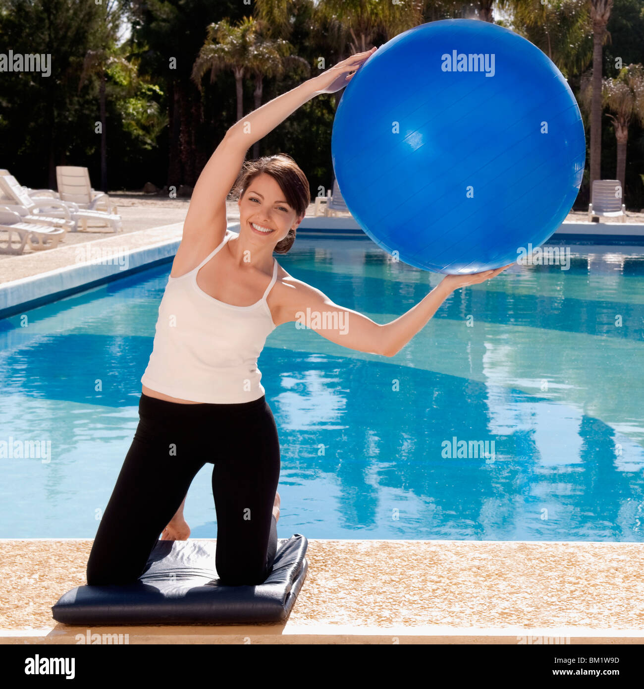 Woman exercising with a fitness ball at the poolside Stock Photo