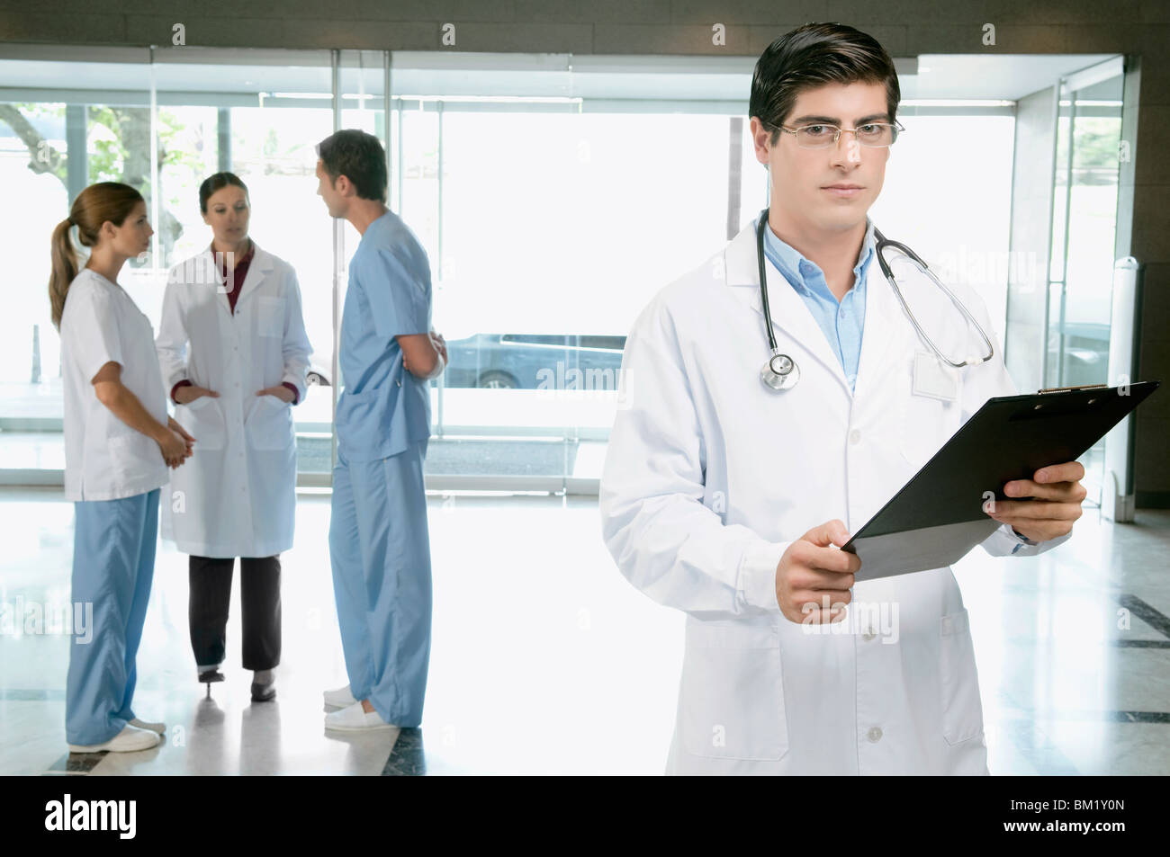 Doctor holding a clipboard with his colleagues discussing in the background Stock Photo