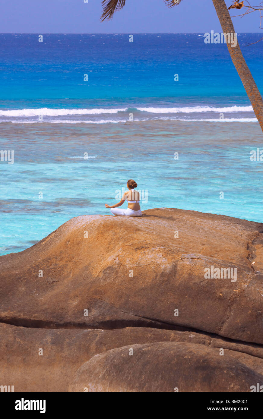 Young woman meditating on rock, Seychelles, Indian Ocean, Africa Stock Photo