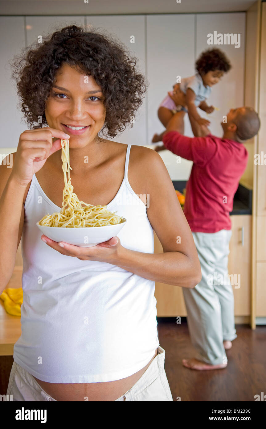 Pregnant woman eating pasta with her family in the background, San