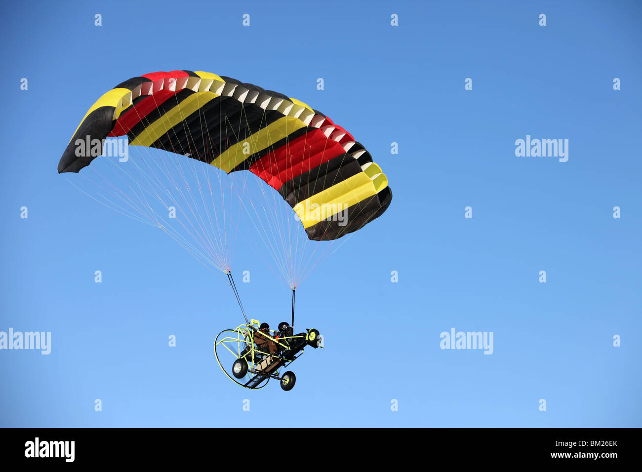 Powered parachute ultra light aircraft flying by in blue sky with pilot and  passenger. Multi colored chute Stock Photo - Alamy
