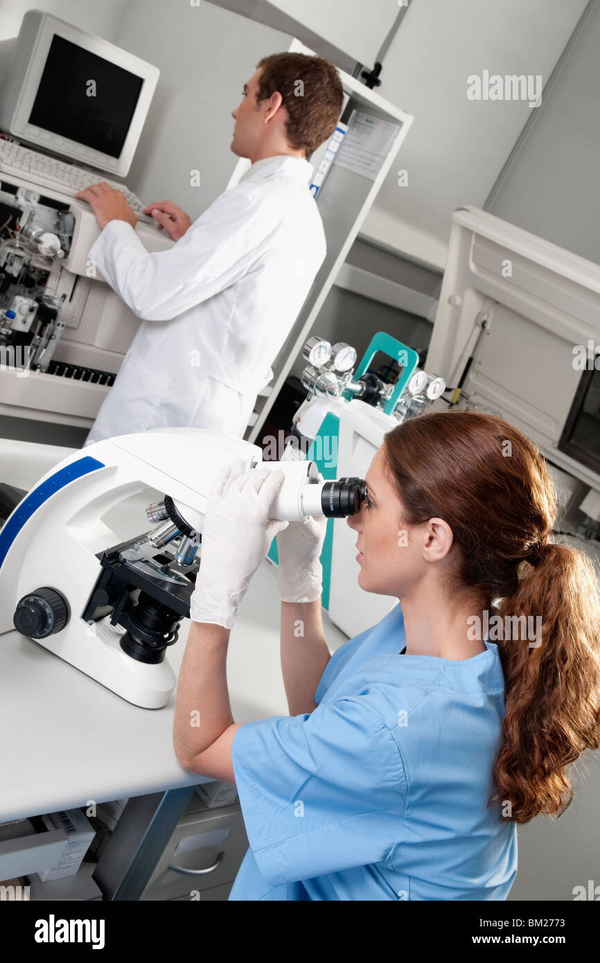 Female lab technician analyzing a sample through a microscope Stock