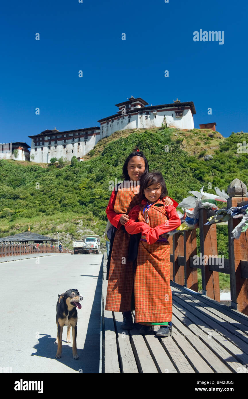 Two girls and dog on a bridge below Wangdue Phodrang Dzong, founded by the Zhabdrung in 1638, Bhutan Stock Photo