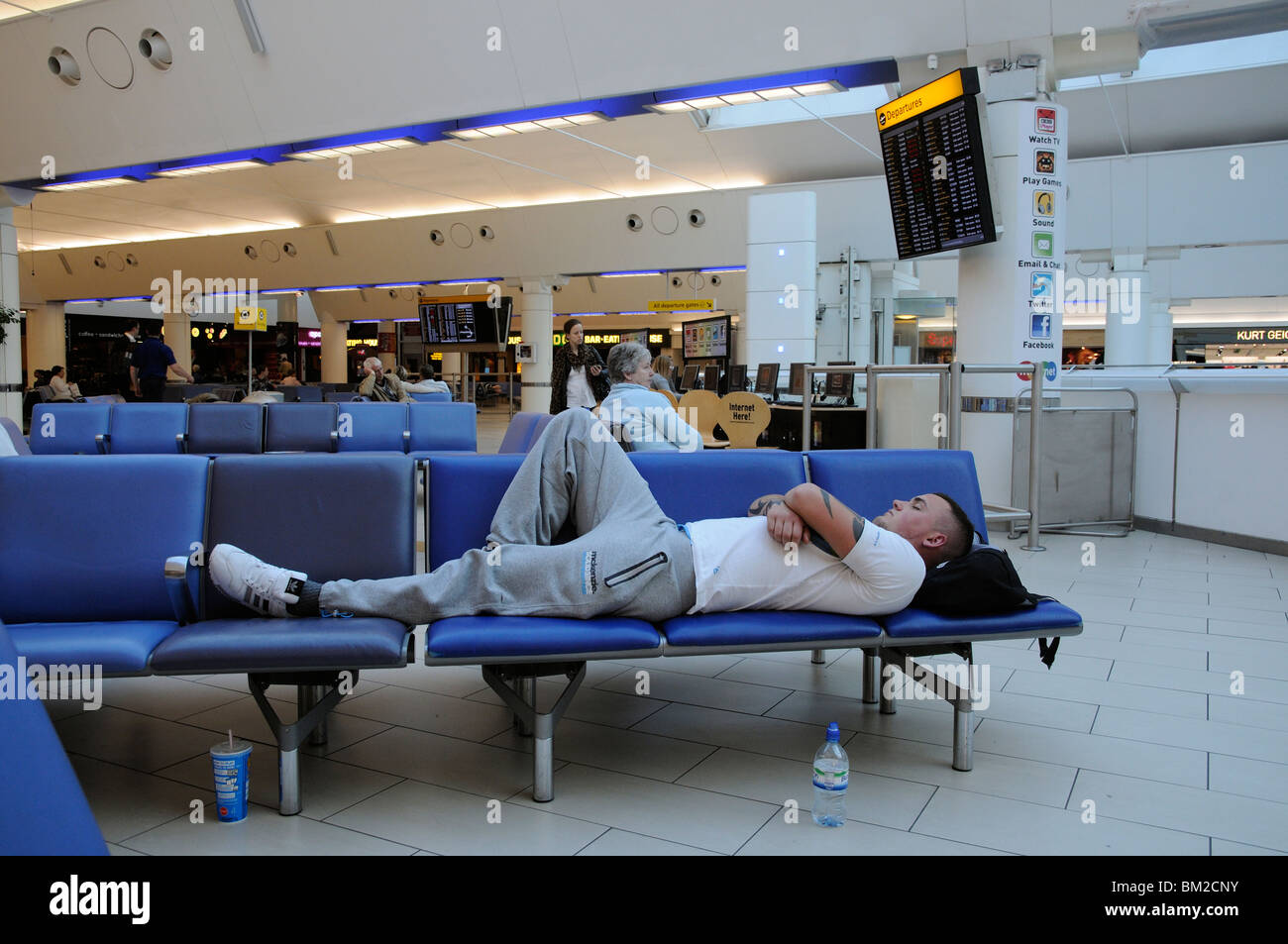 Passenger laying across seats in the Departure Lounge South terminal Gatwick Airport England UK Stock Photo
