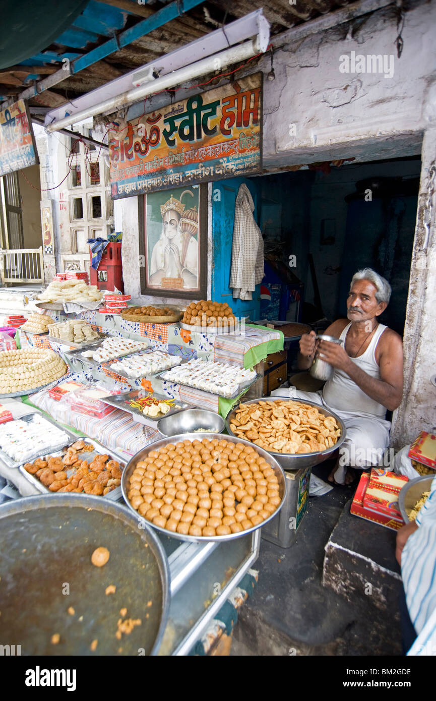 Diwali sweet stall with stallholder and picture of the Hindu god, Hanuman, Udaipur, Rajasthan, India Stock Photo