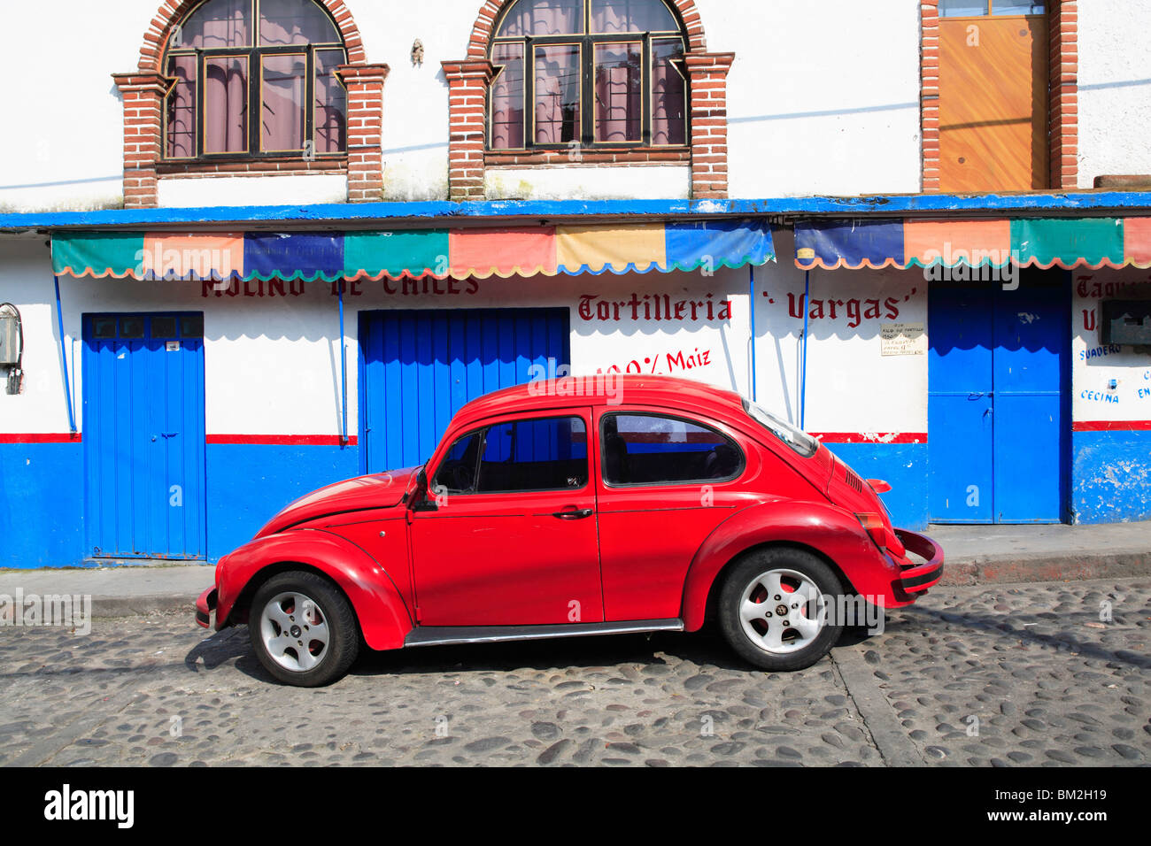 Red Volkswagon Beetle parked on cobblestone street, Tepoztlan, Morelos, Mexico Stock Photo