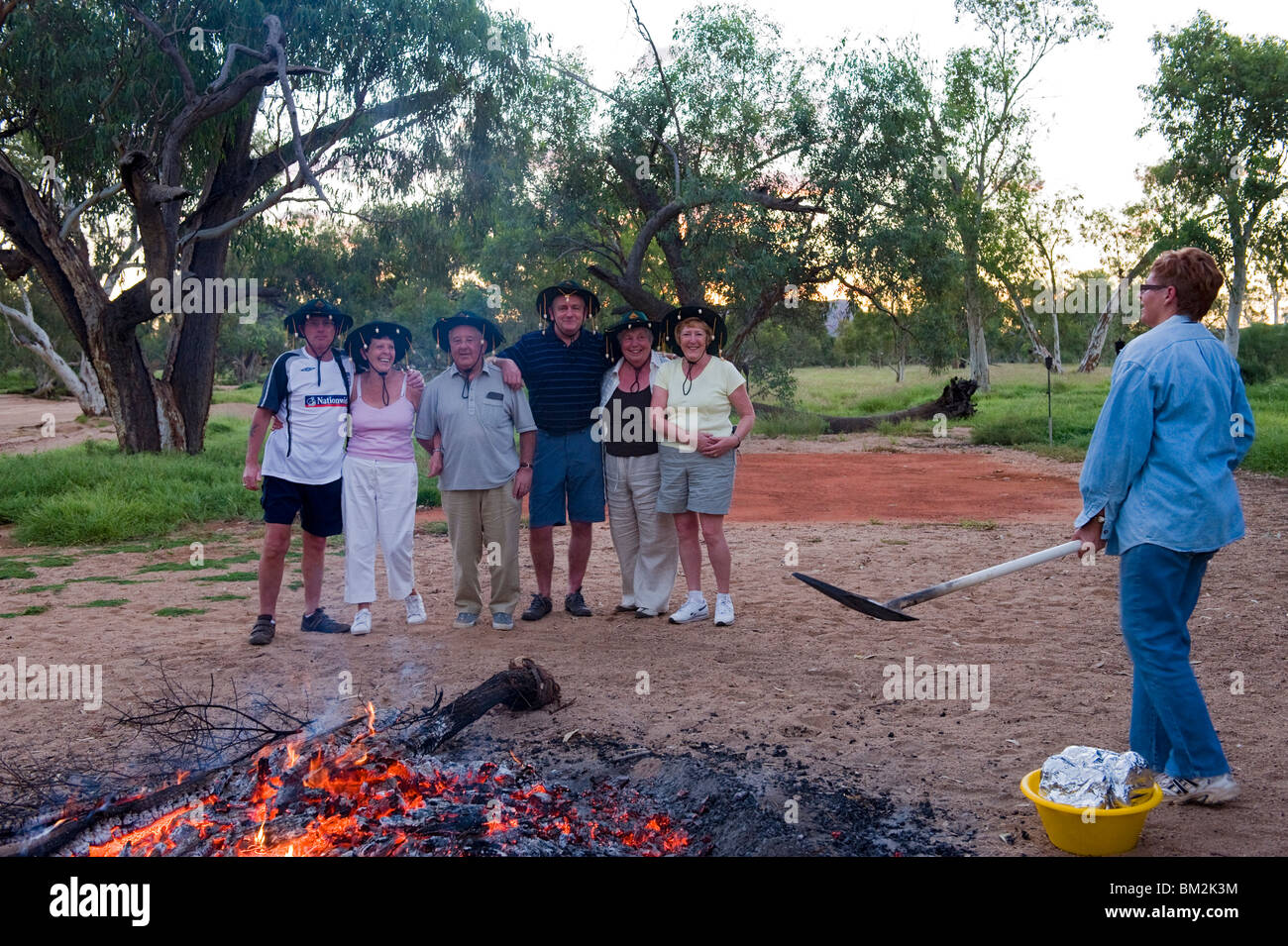 A group of tourists wearing corked hats and watching the fire and barbecue preparations Stock Photo