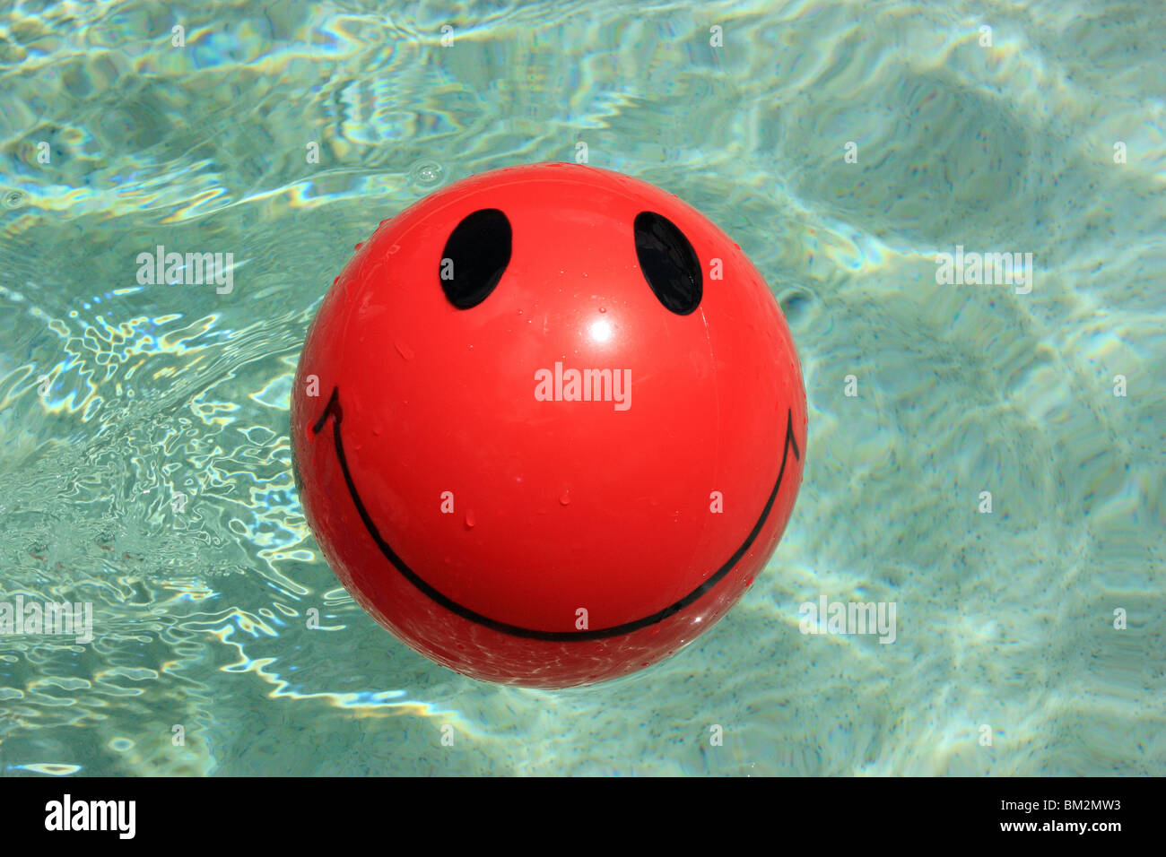 RED BALL WITH BLACK SMILEY FACE DESIGN FLOATING IN SWIMMING POOL BDA