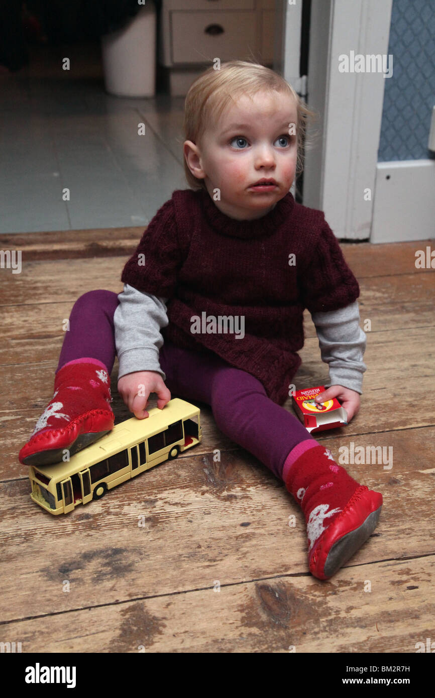 TODDLER, PLAYING, FLOOR: A two year old baby girl toddler child playing with toy bus with a box of sweets in socks and boots model released Stock Photo